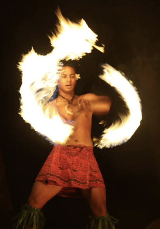 Performer spinning fire poi, with flames creating circular patterns around them against a dark background.