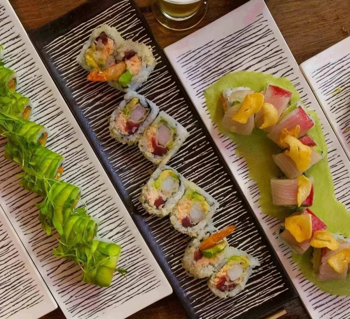 Assorted sushi rolls on black and white plates, with a small glass of green tea in the background.