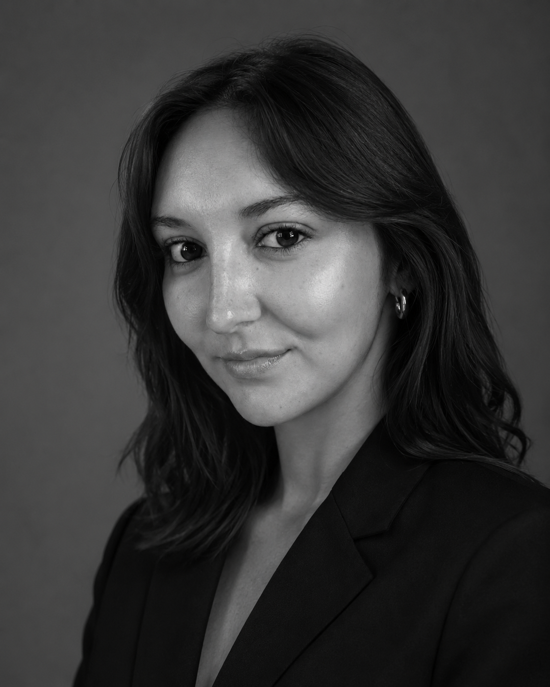 Black and white portrait of a woman with shoulder-length dark hair, wearing a blazer and small hoop earrings, facing slightly to the right with a subtle smile.