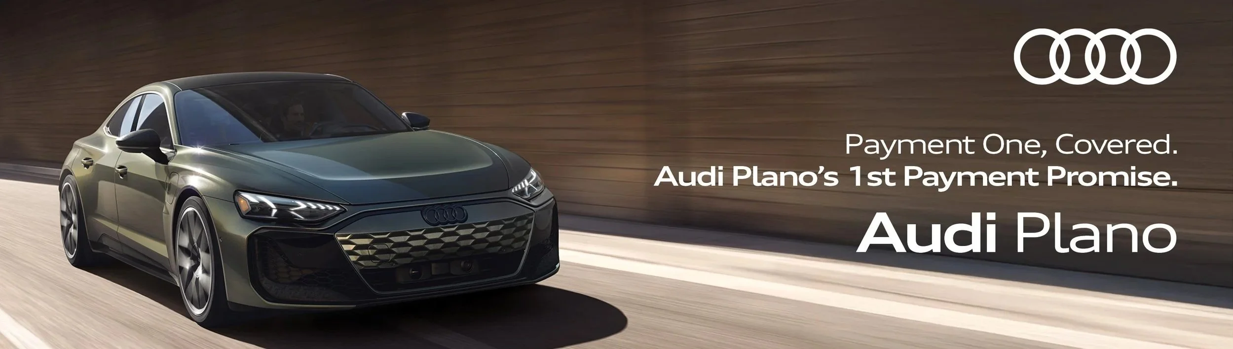 A sleek, green Audi car driving on a road with a wooden fence in the background, along with the Audi logo and promotional text about Audi Plano's first payment promise.