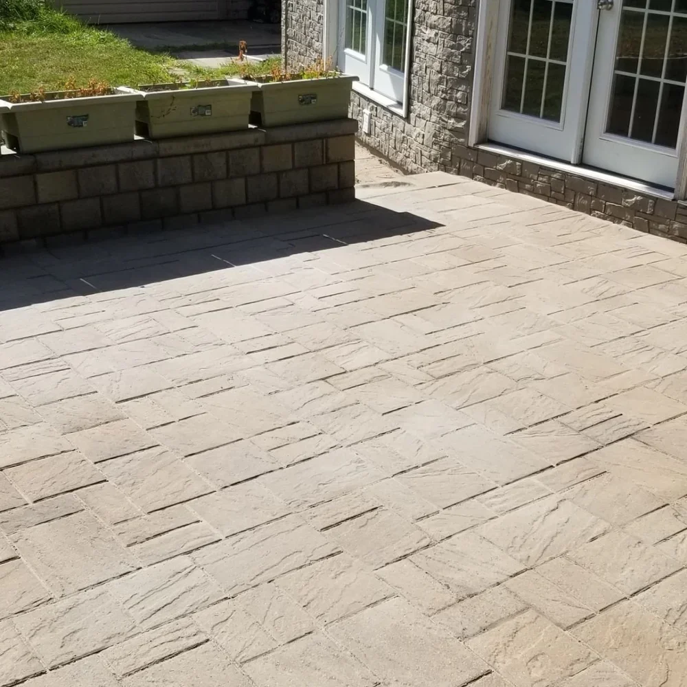A backyard patio with light-colored stone pavers, a brick wall, and a white door with glass panels.