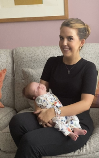 A woman sitting on a sofa holding a sleeping baby in her lap.