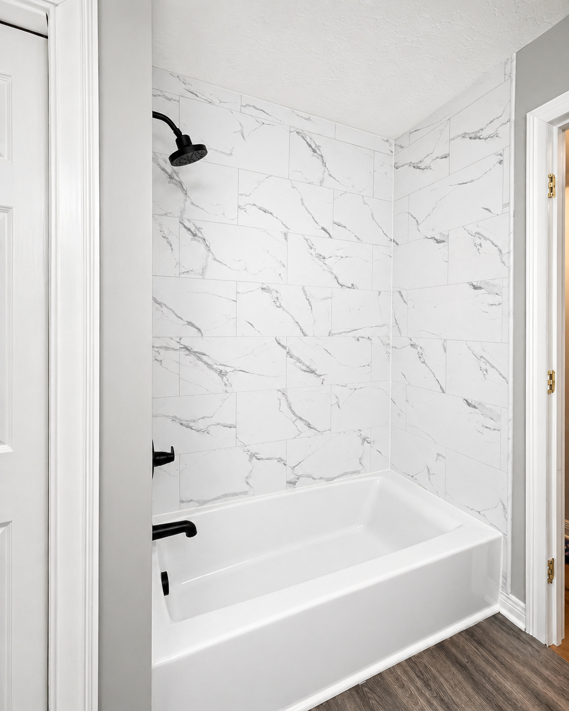 Bathroom remodel featuring white bathtub, marble-look shower tile, matte black fixtures, gray walls, and wood-look flooring.