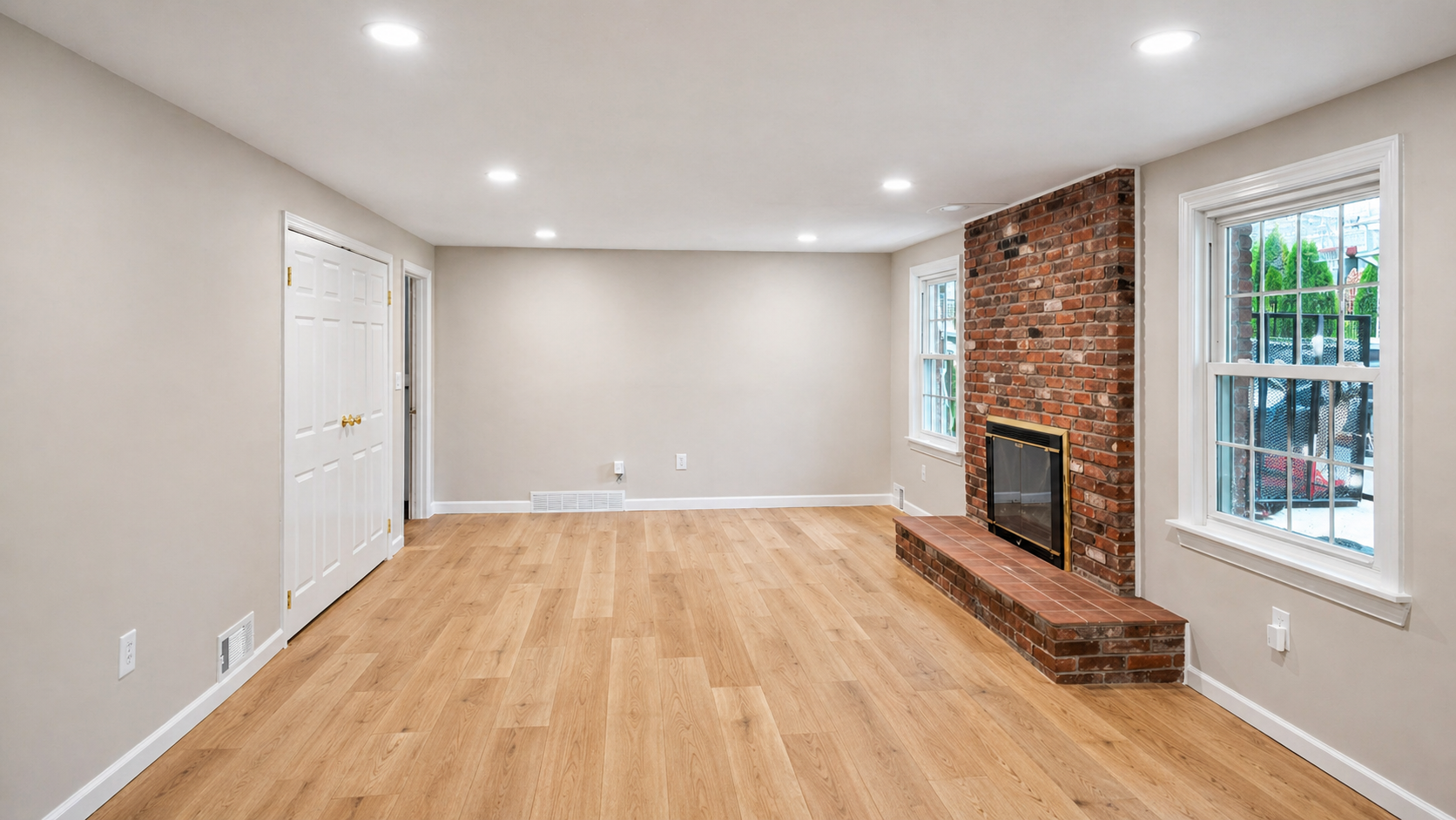 Basement remodel featuring an open family room layout, brick fireplace, recessed ceiling lights, updated flooring, and bright neutral finishes.