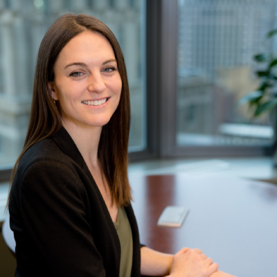 Founder Chelsea Pritchard, a woman with long brown hair, smiling, sitting at a desk in an office with large windows and cityscape view.