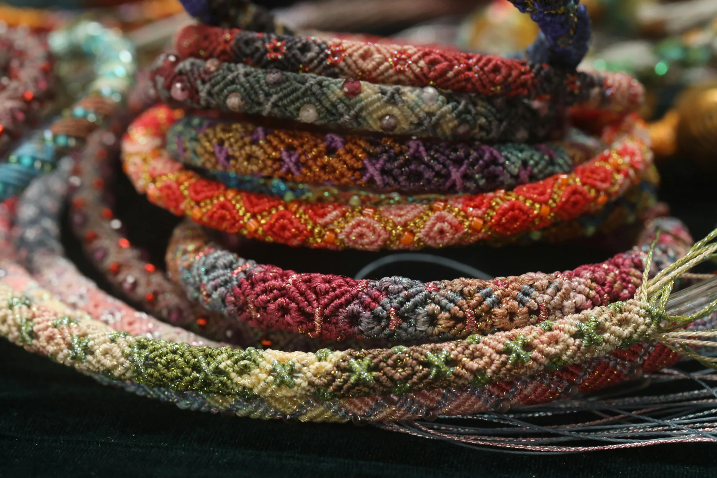 Colorful beaded and embroidered fabric bracelets stacked together with various intricate patterns and sparkling embellishments.