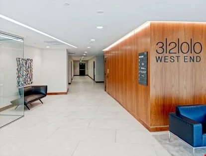 Lobby area with a wood-paneled wall displaying the words 'Oloslo West End', a black bench, and a blue armchair.