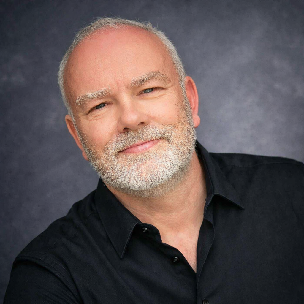 Portrait of a smiling, middle-aged man with a beard, wearing a black shirt, against a grey background.