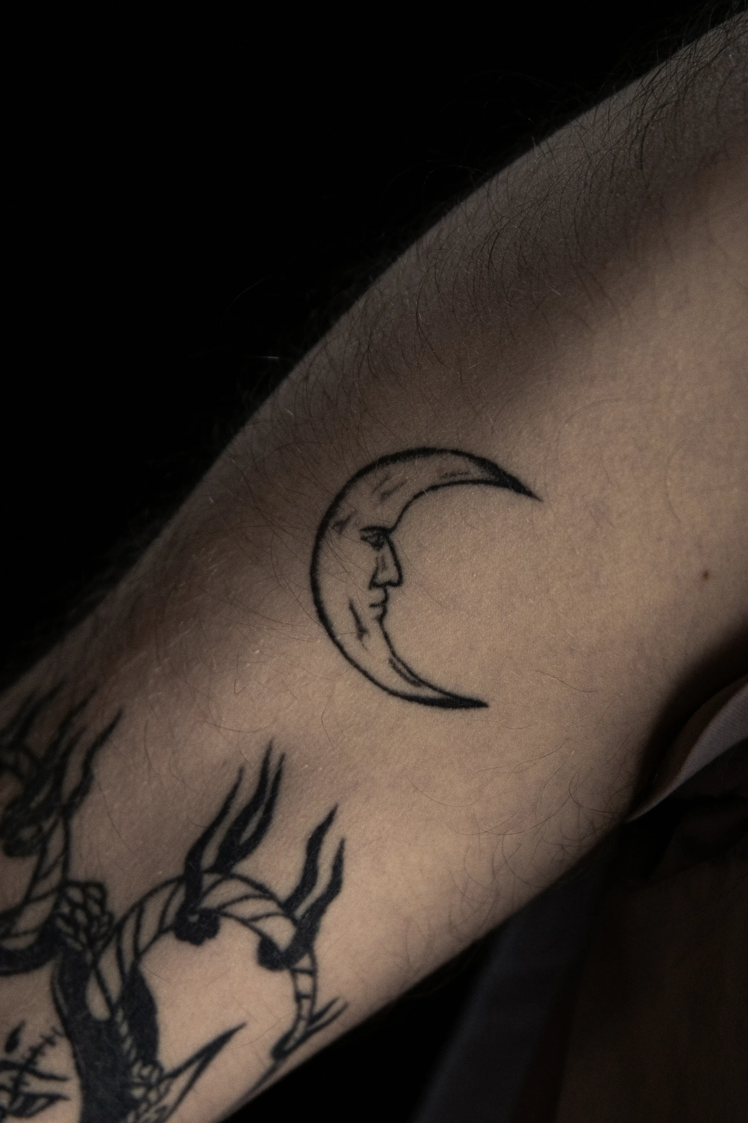 Tattoo eines Mondes mit einem Gesicht auf einer menschlichen Haut.
