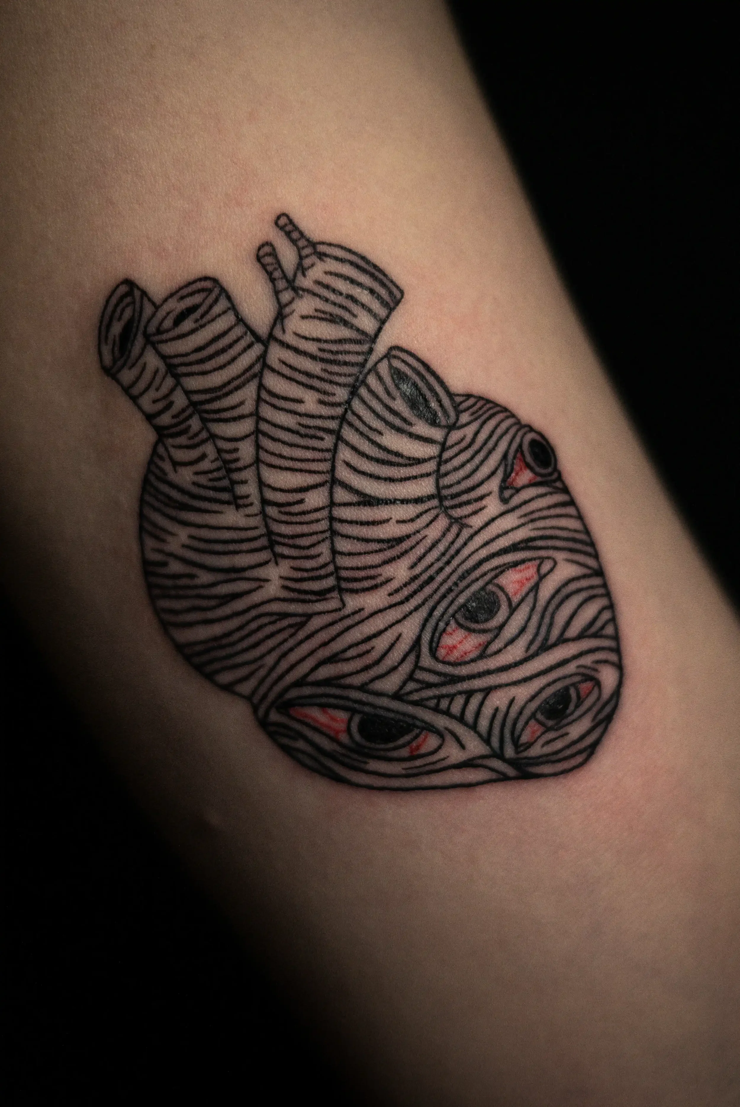 Tattoo eines stilisierten Gesichts, bestehend aus schwarzen Linien und roten Akzenten, auf der Haut.