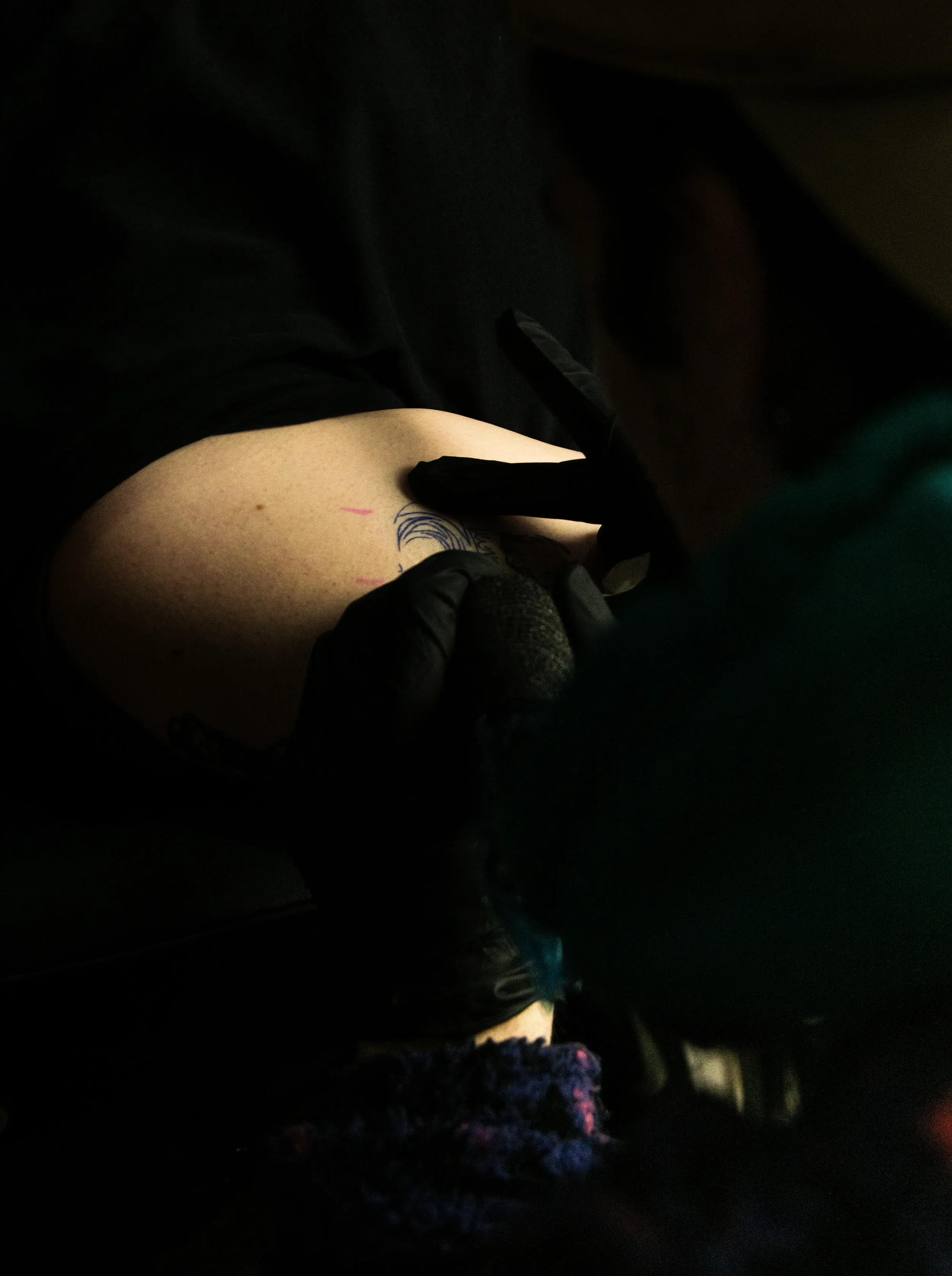 Nahaufnahme einer Person mit einem gefärbten Tattoo auf der Haut, die von einer Person mit schwarzen Handschuhen gestochen wird.