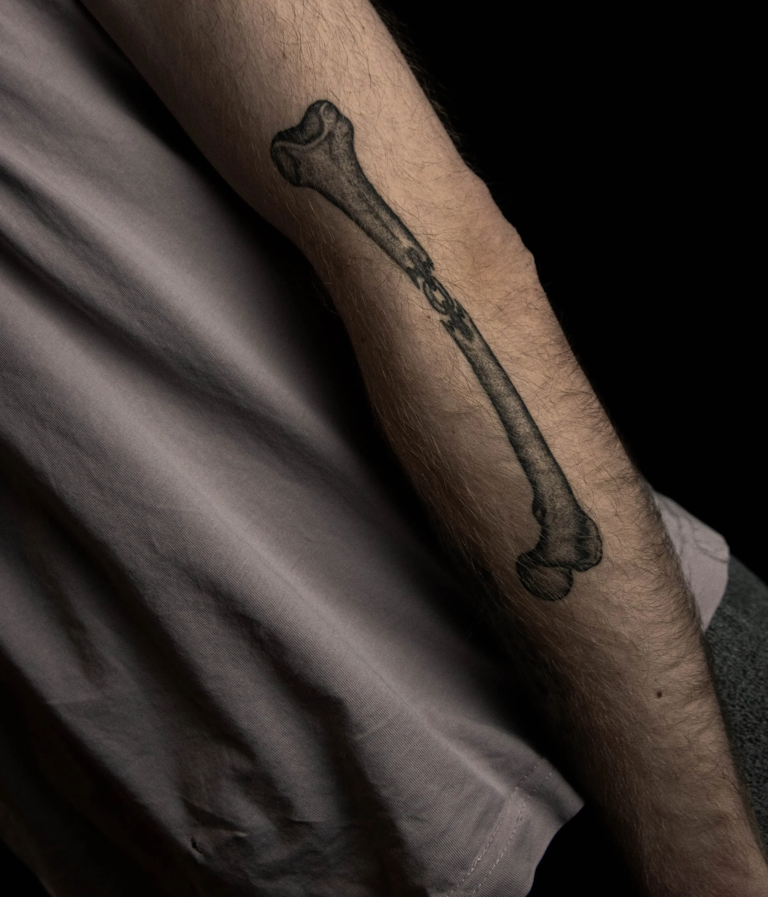 Nahaufnahme eines Arms mit einer Tätowierung eines Knochen-Designs, umgeben von heller Haut und dunklem Hintergrund.