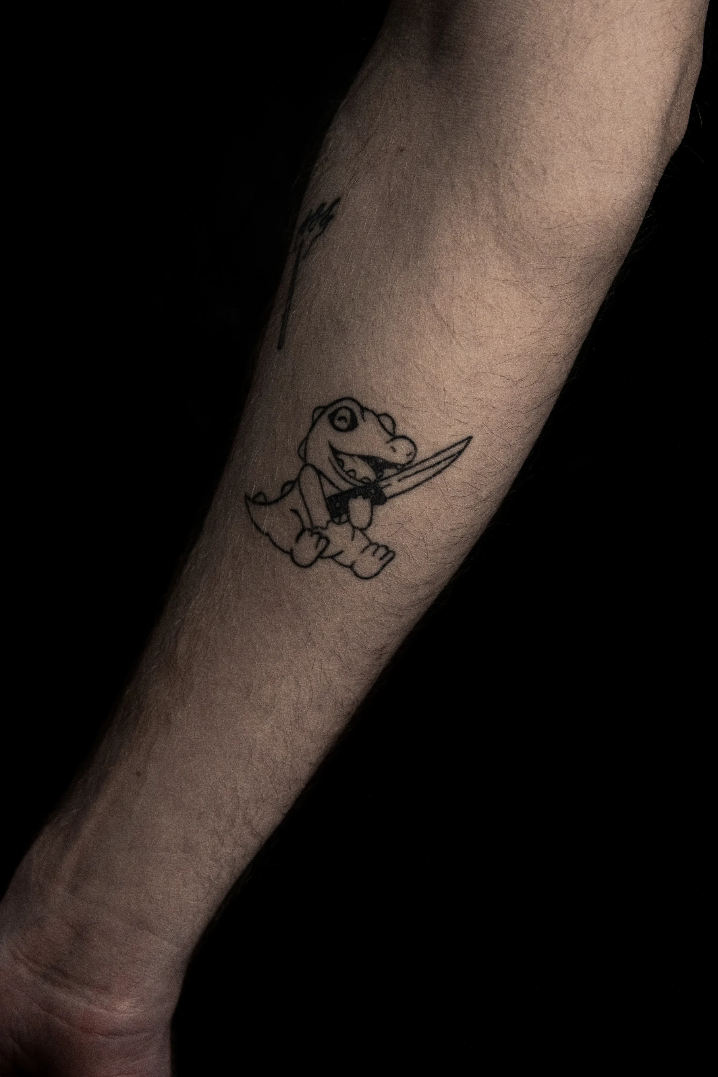 Tattoo eines Dinosauriers mit Messer auf dem Arm.