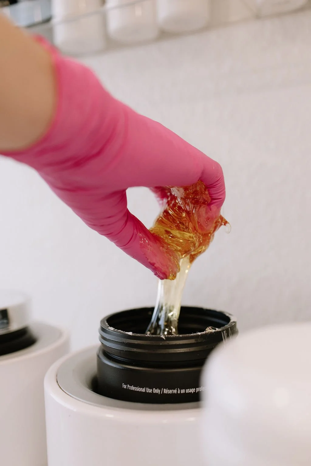 A person wearing pink gloves handling a piece of amber-colored resin or wax over a heat source in a laboratory or professional setting.