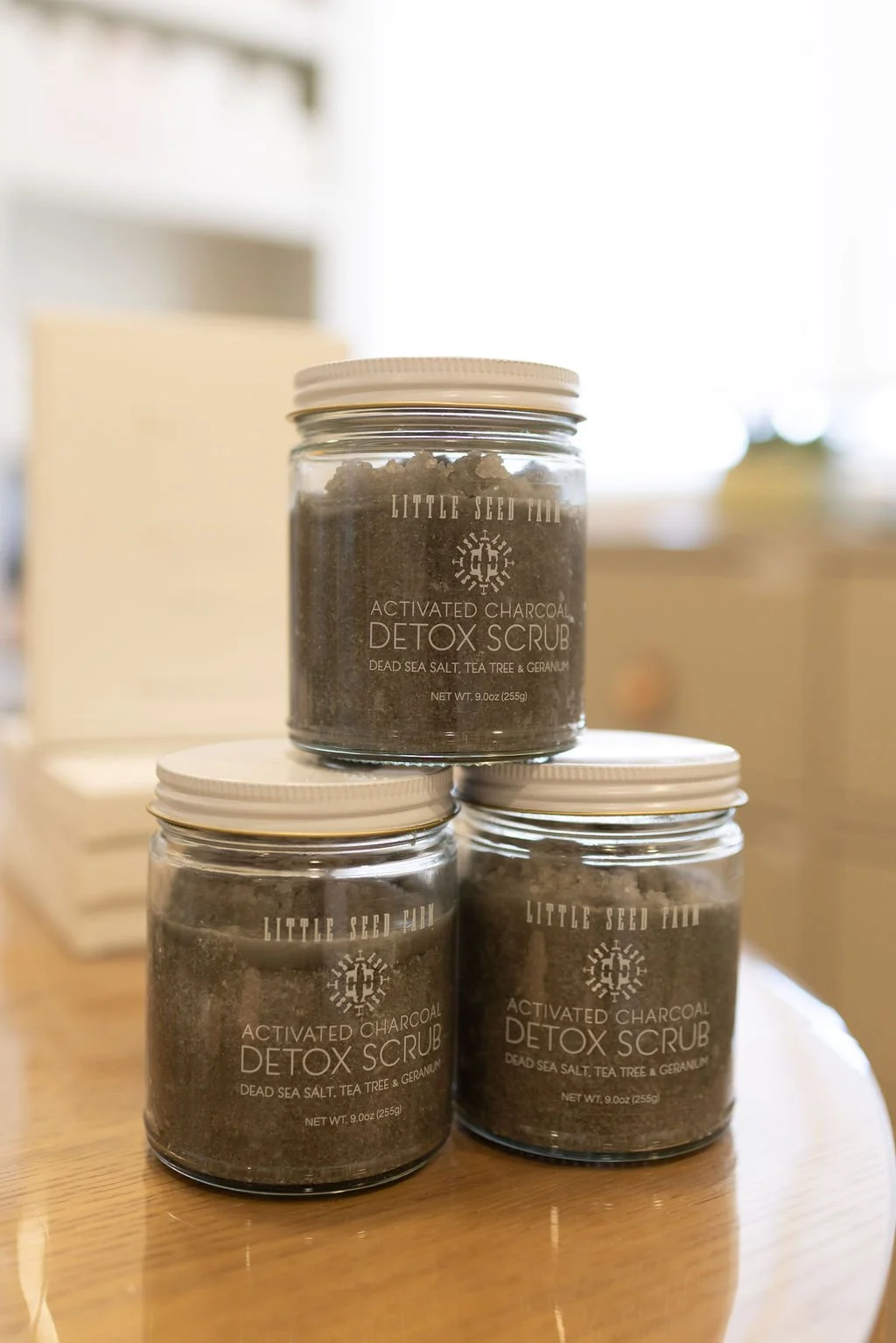 Three jars of activated charcoal detox scrub on a wooden surface in a home setting.