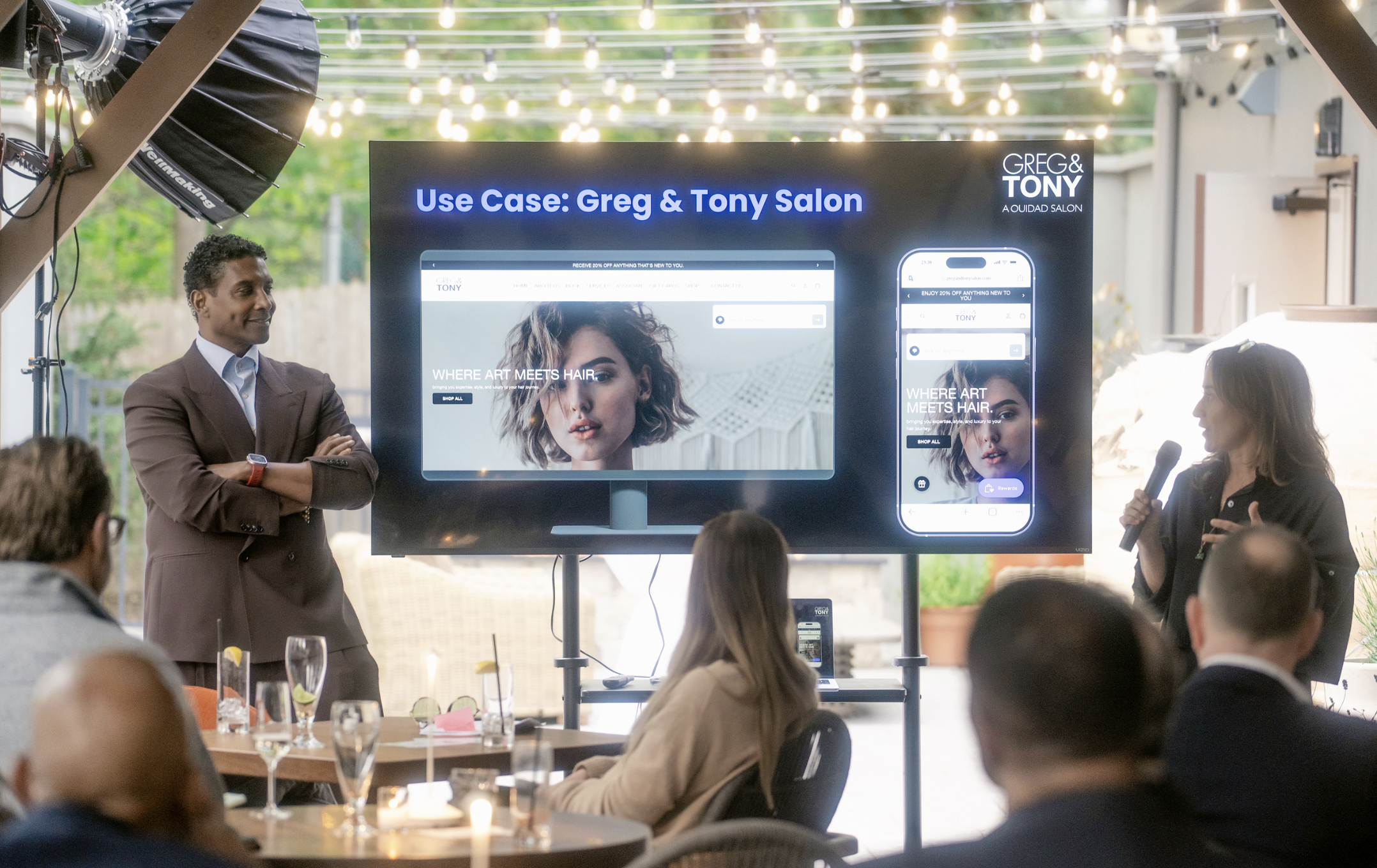 Presentation at an event titled 'Use Case: Greg & Tony Salon,' with Jay Norris standing near a large screen displaying a website and a smartphone mockup, surrounded by an audience.