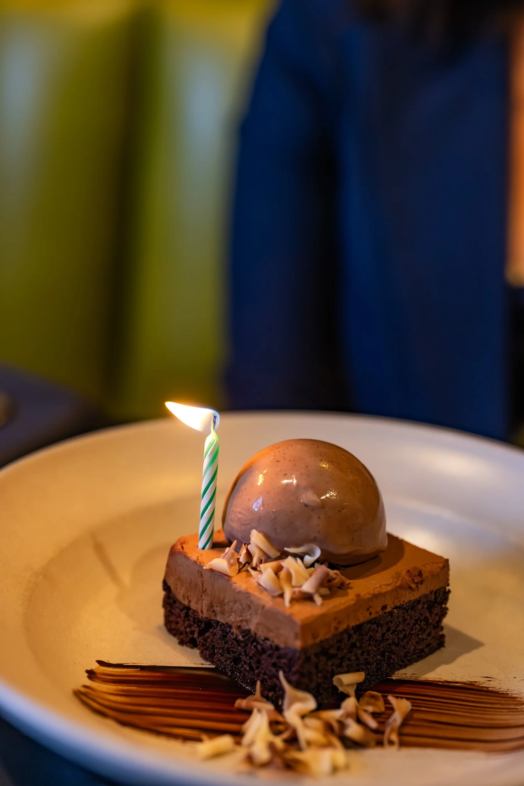 Chocolate dessert topped with a scoop of ice cream and chocolate shavings, with a lit birthday candle on a yellow plate.