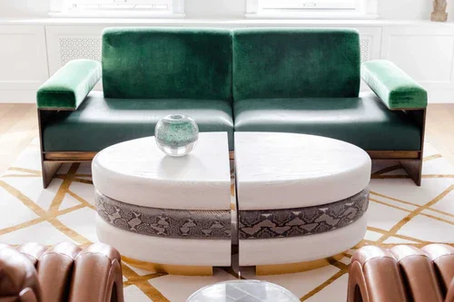 Modern sofa with green velvet back and armrests, and a white oval-shaped coffee table with a snakeskin patterned band in a living room.
