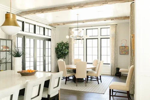 Bright dining area with large windows, a round table with chairs, and a chandelier, in a modern home.