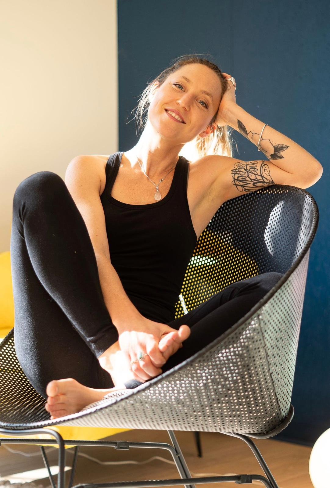 Une femme souriante relaxée assise dans une chaise moderne avec un fond blanc et bleu.