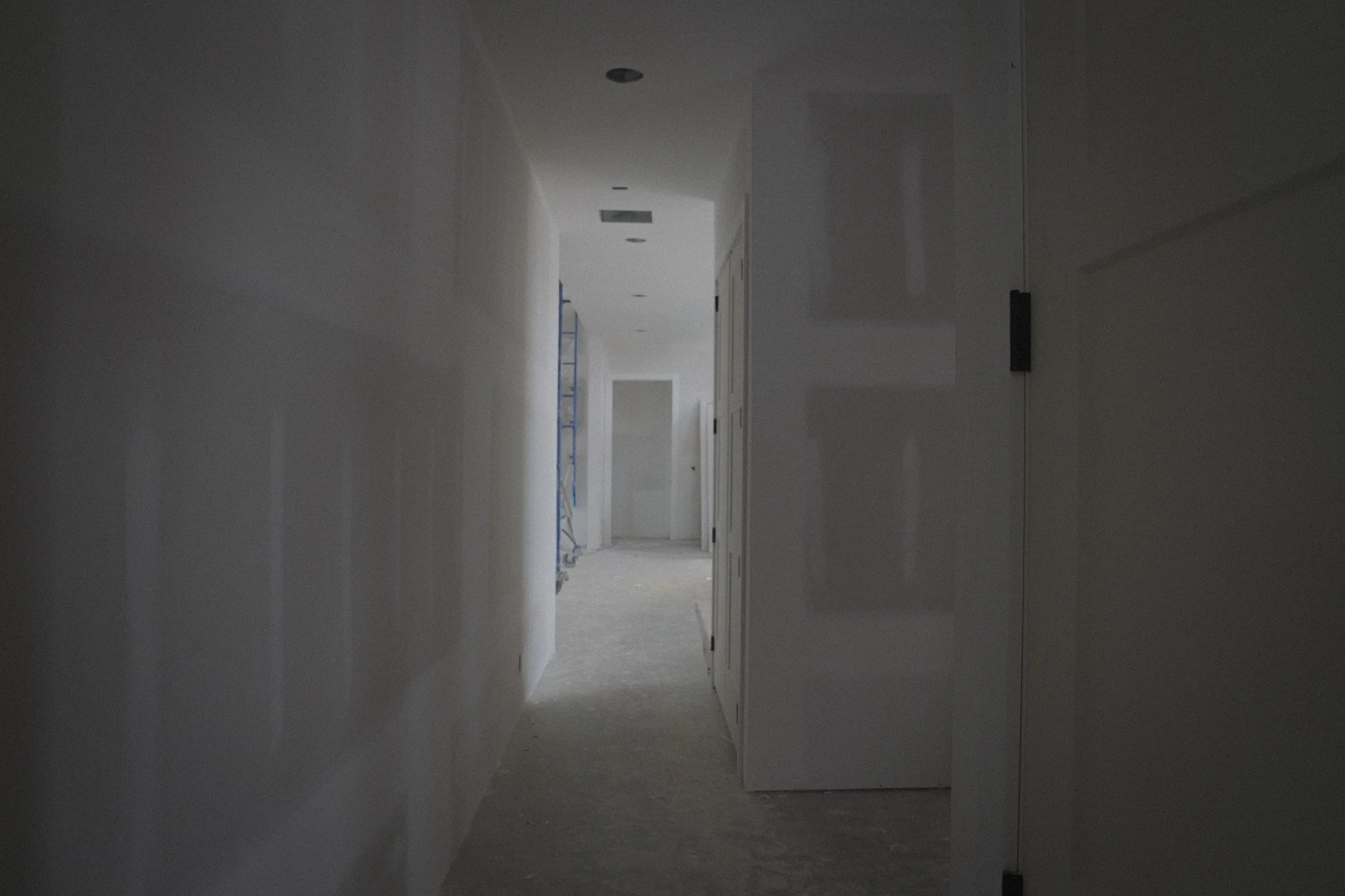 Hallway in a house under construction or renovation, with doors and a scaffold visible at the end.