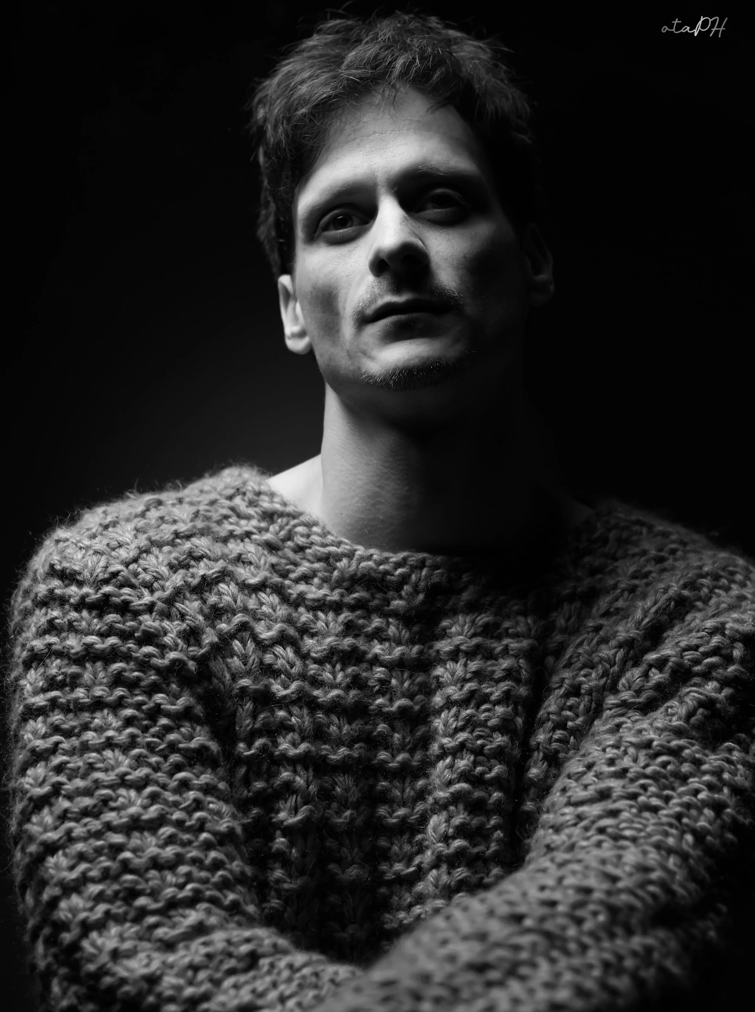 Ritratto in bianco e nero di un uomo con capelli corti, barba sottile e indossando un maglione di lana spessa.