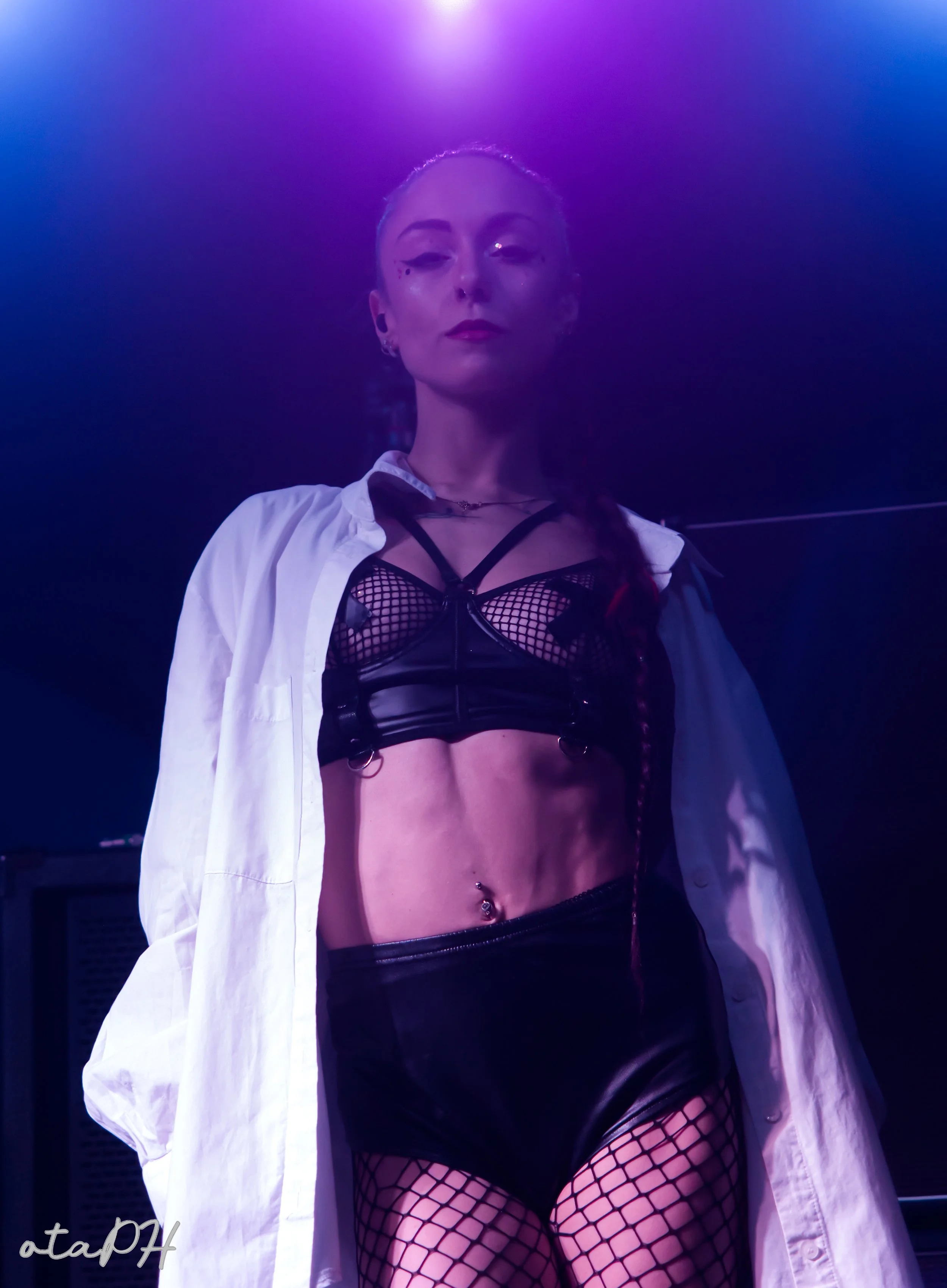 Una donna in abbigliamento sexy ricoperta di luce viola e blu, indossa una camicia bianca aperta, un top nero in rete e calze a rete.
