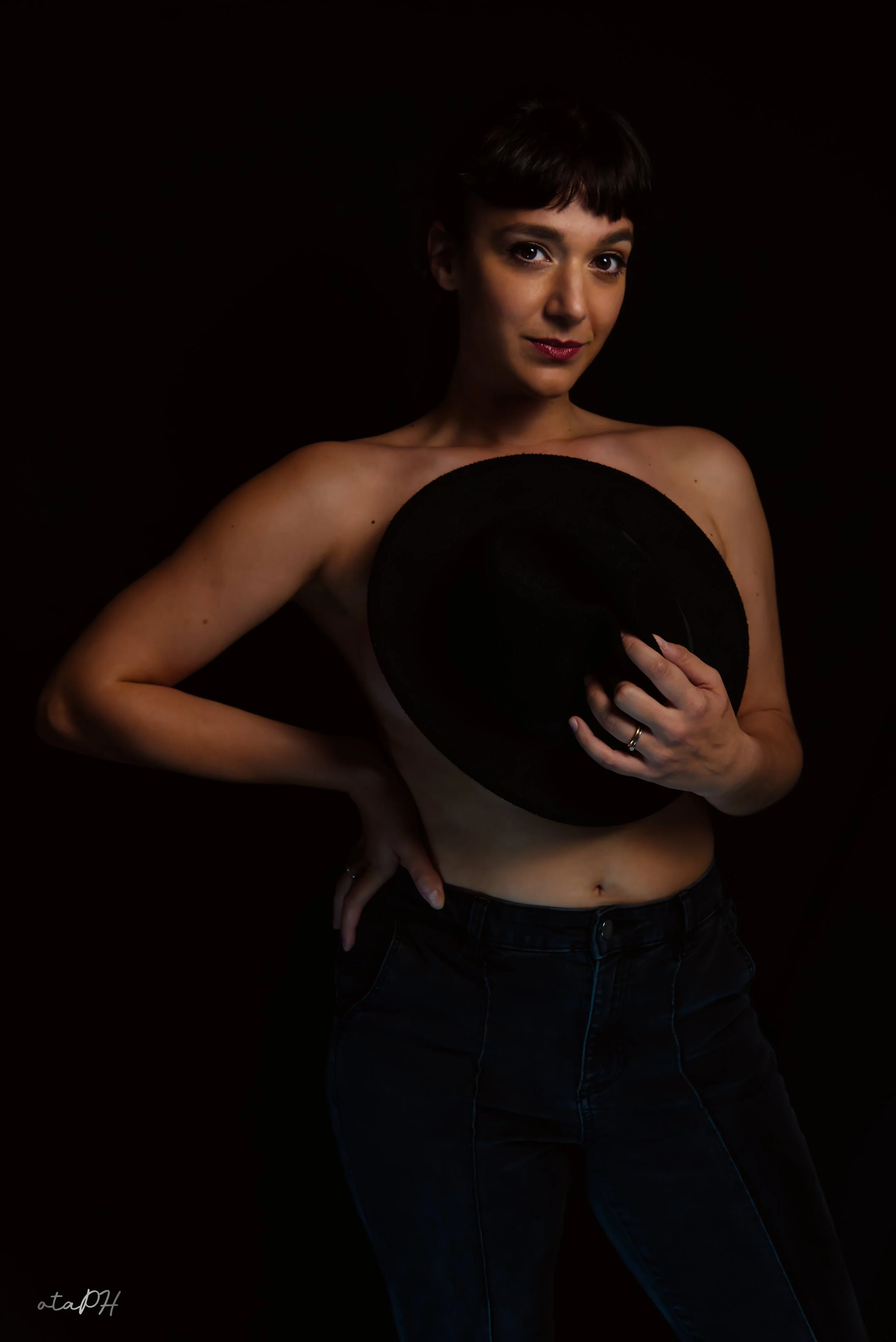 Donna con abbigliamento casual, con un cappello nero in mano, sullo sfondo nero.