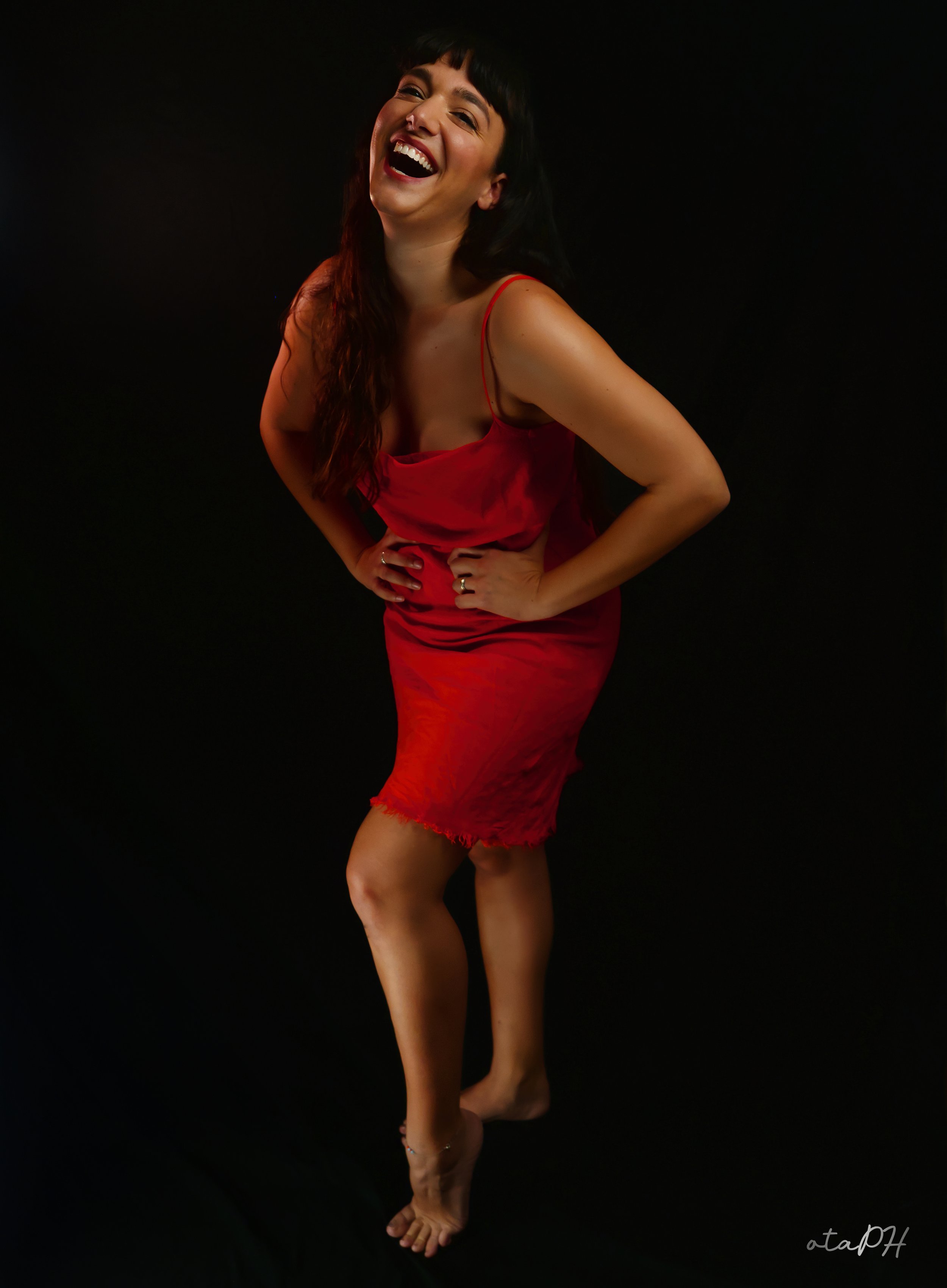 Donna con capelli scuri e sorriso, indossa un vestito rosso e si trova contro uno sfondo nero.