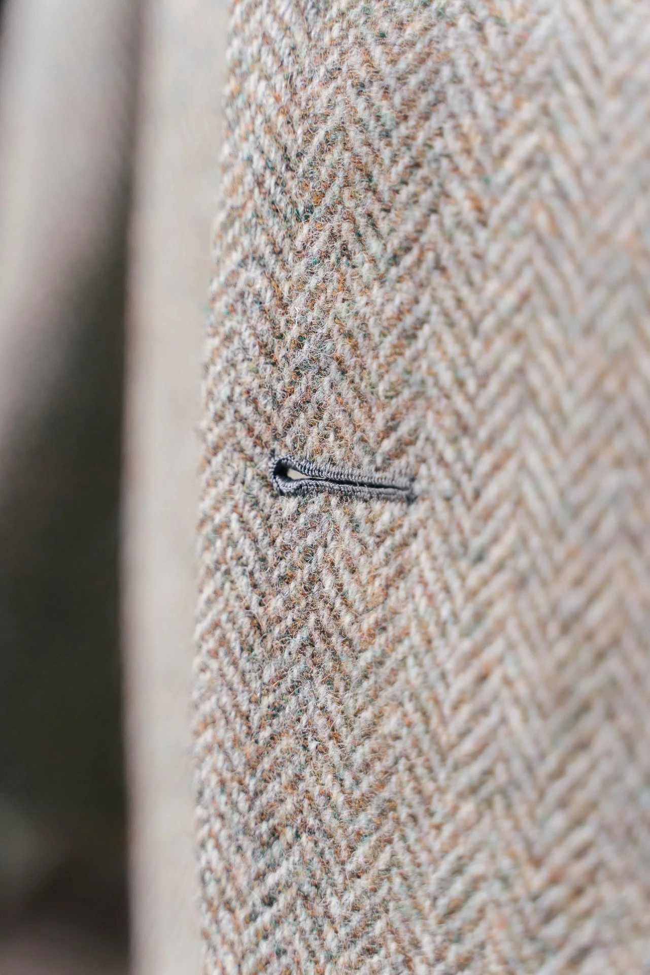 Close-up of a textured beige and brown tweed fabric with a small black zipper pocket.