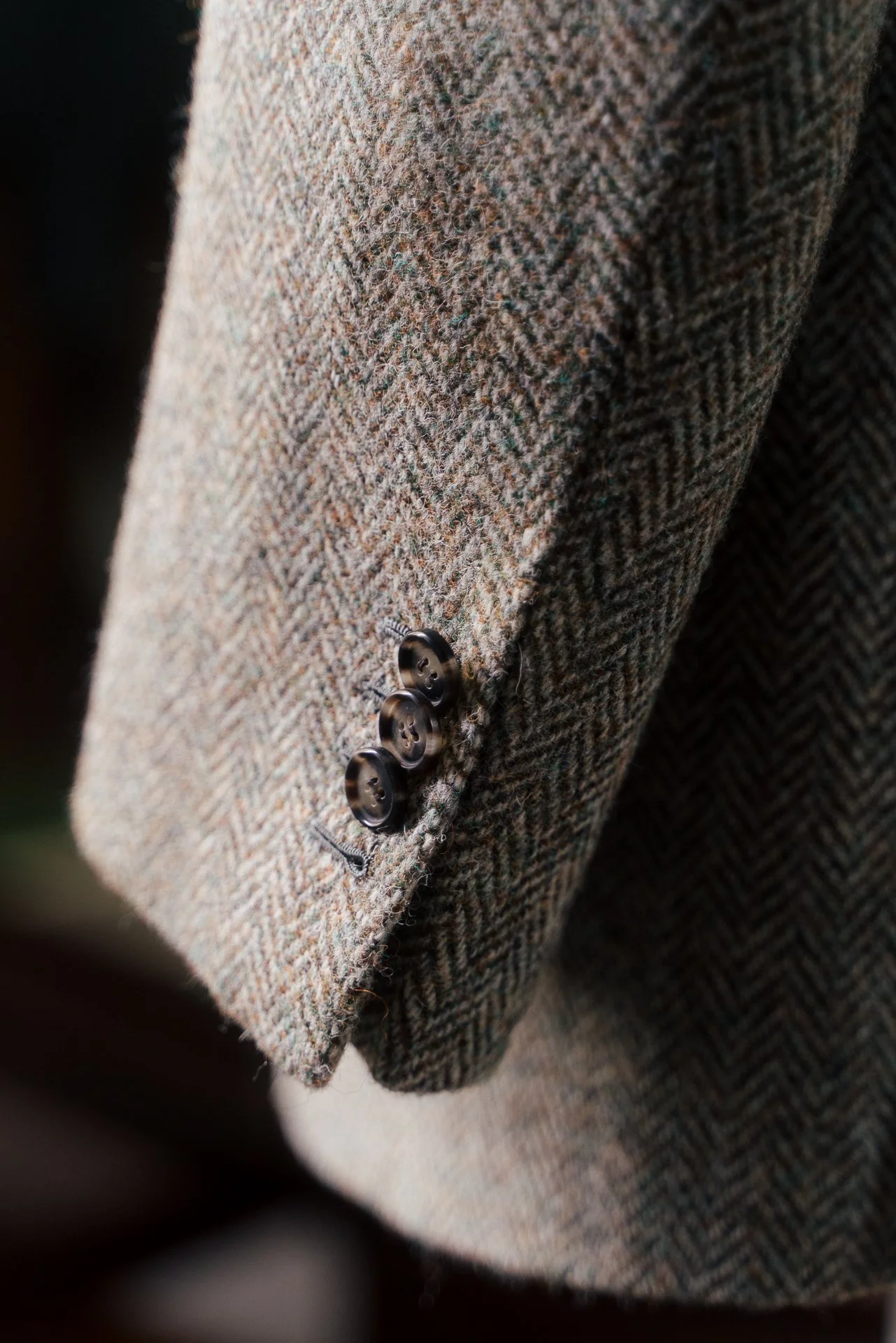 Close-up of a brown tweed blazer sleeve with four dark buttons.