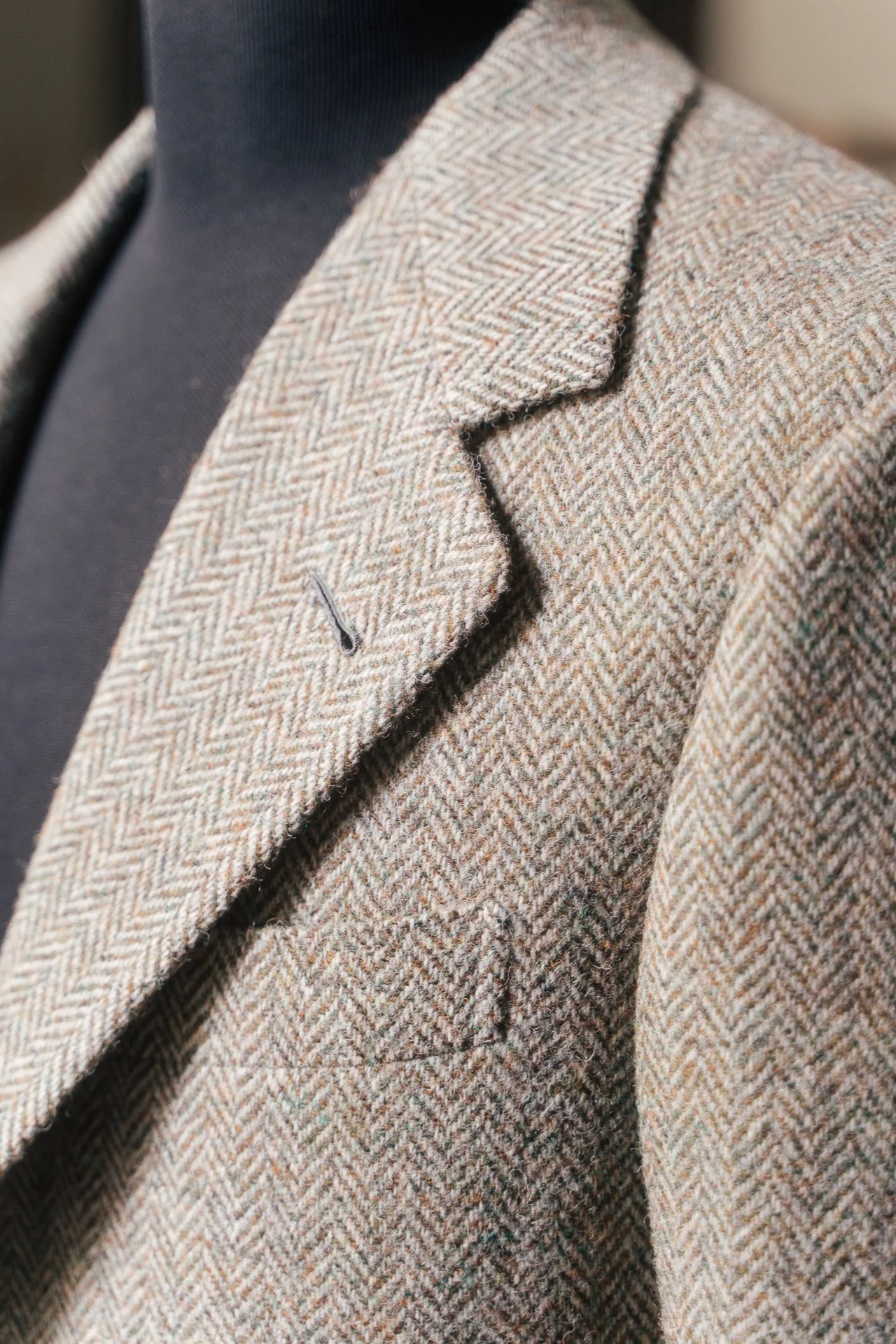 Close-up of a herringbone-patterned tweed blazer with a notched lapel, worn over a dark shirt.