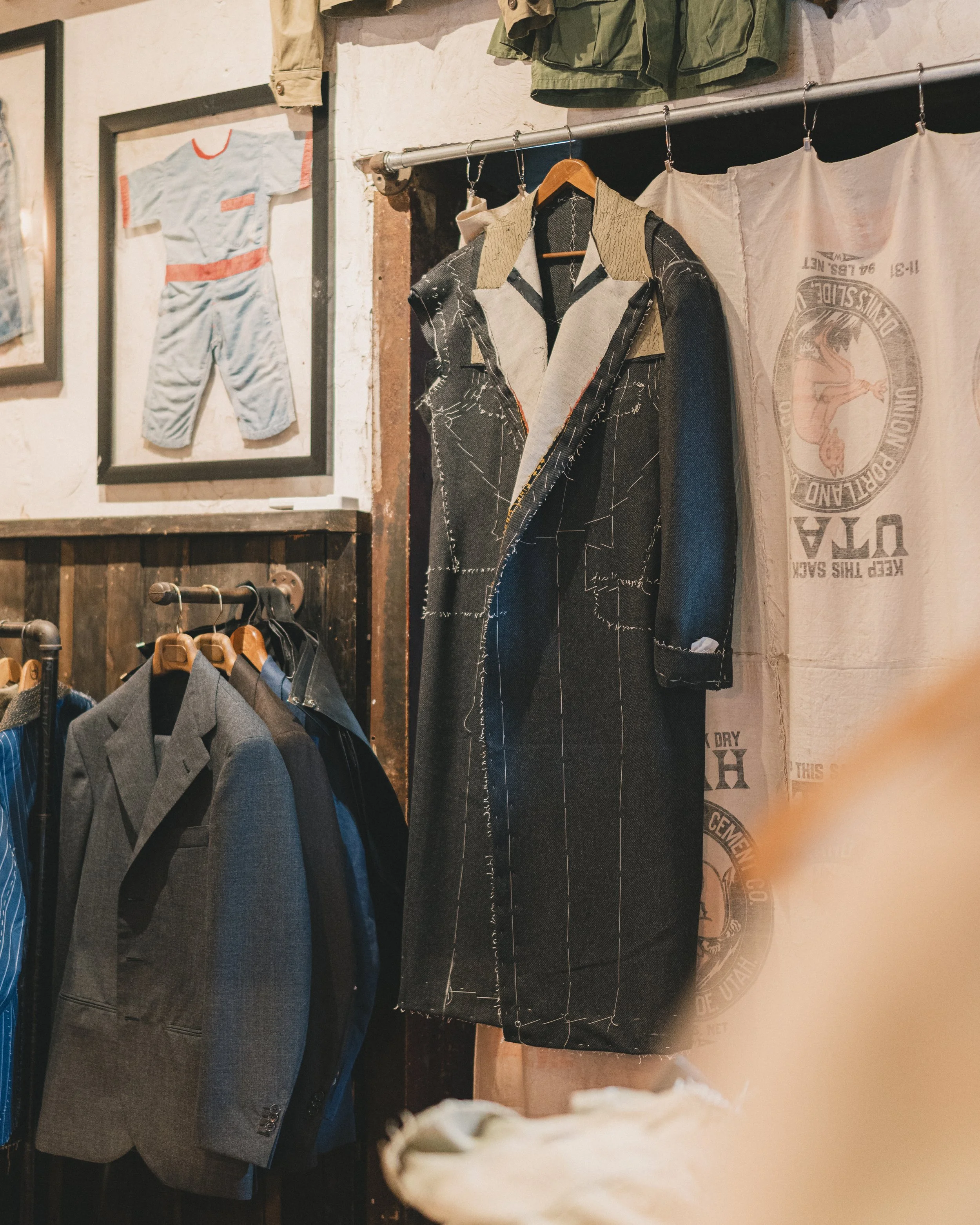 Display of clothing items in a store, including a framed vintage sports outfit, a patterned jacket on a hanger, and a fabric wall hanging with printed text and logo.