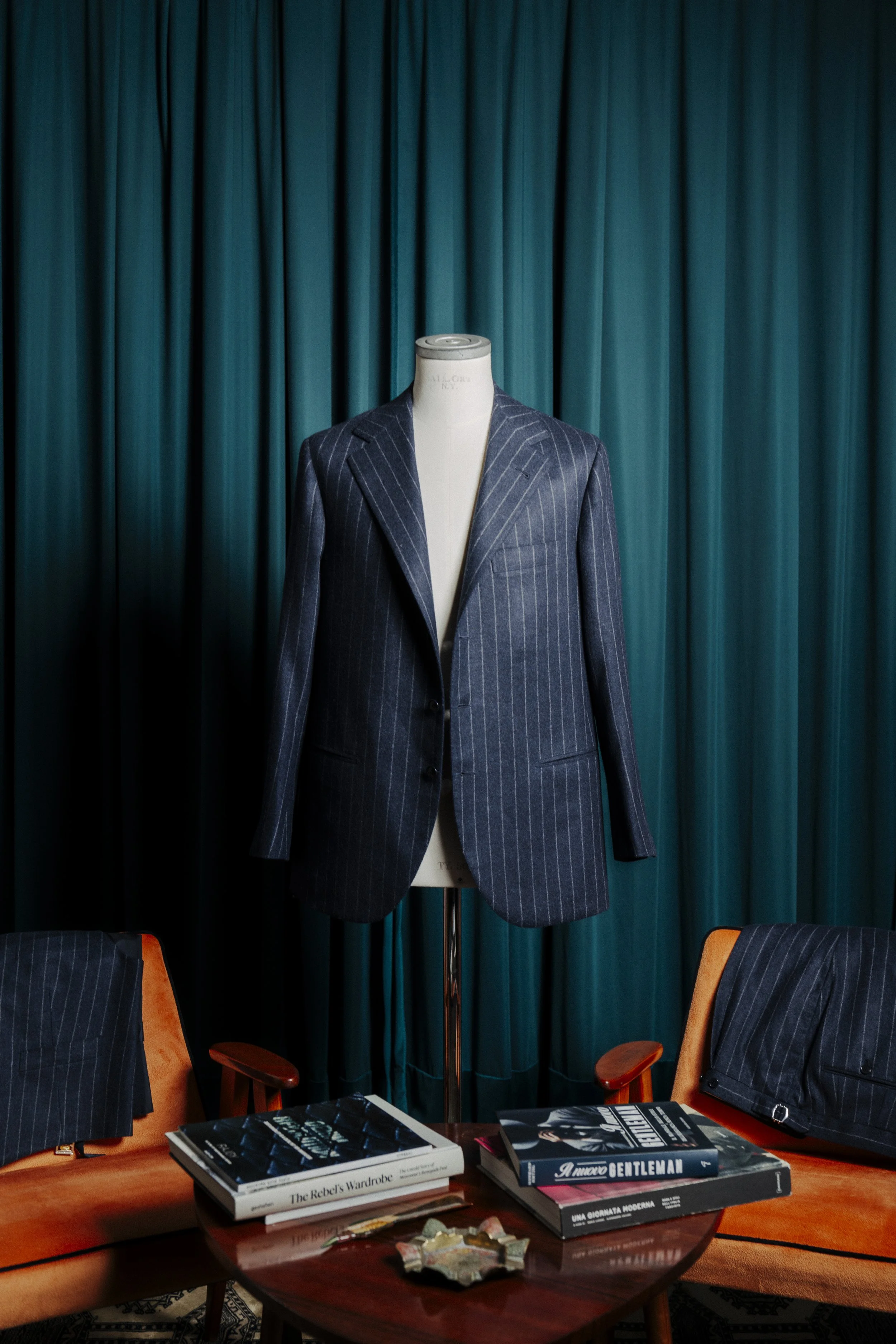 A suit jacket on a mannequin, blue with pinstripes, displayed against a green curtain backdrop.