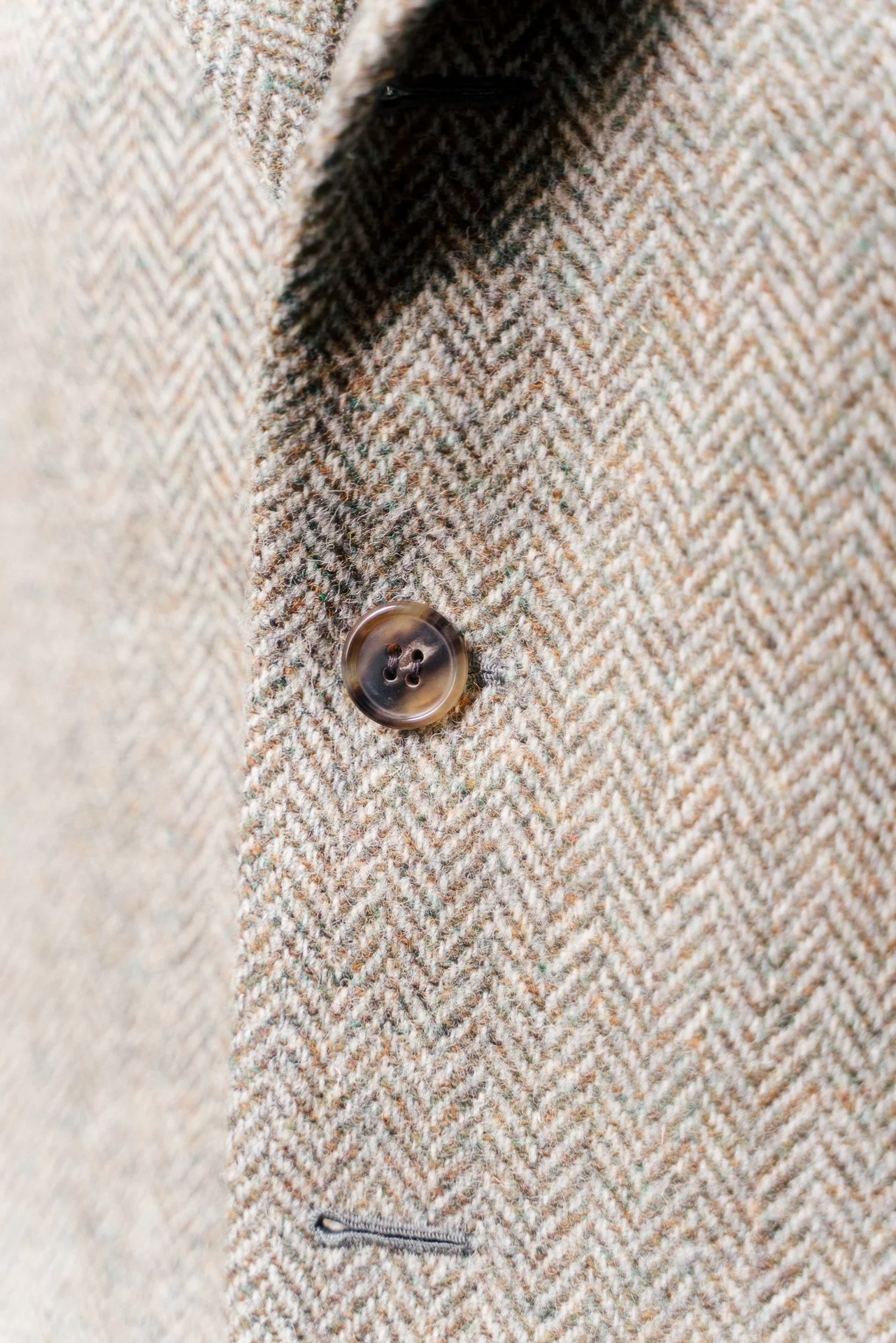 Close-up of a herringbone patterned brown and beige wool coat with a dark button and a zippered pocket.