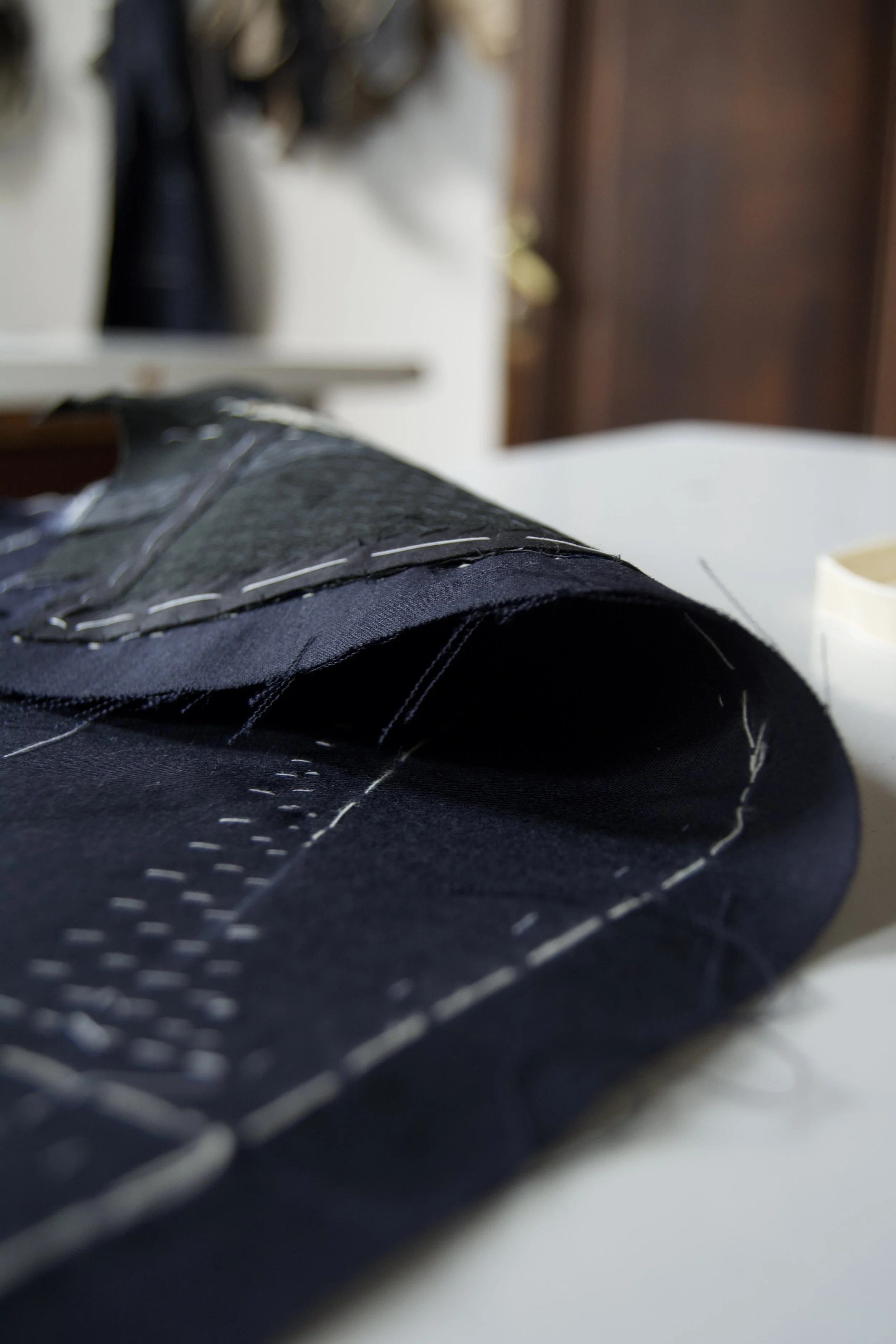 Close-up of black fabric with white stitching, likely part of clothing or upholstery, on a white surface with blurred background.