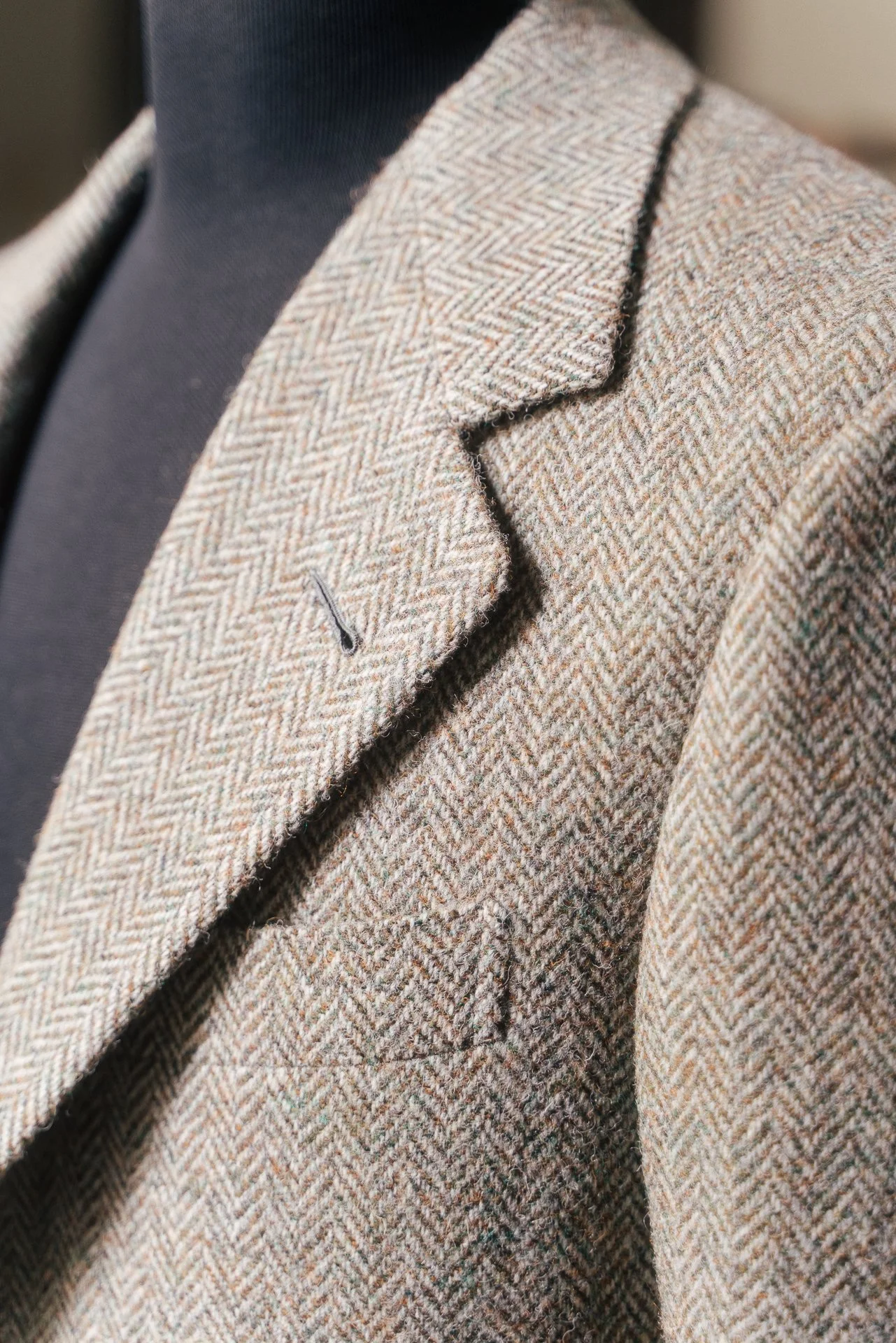 Close-up of a beige and brown plaid wool blazer with a notch lapel, worn over a dark shirt.