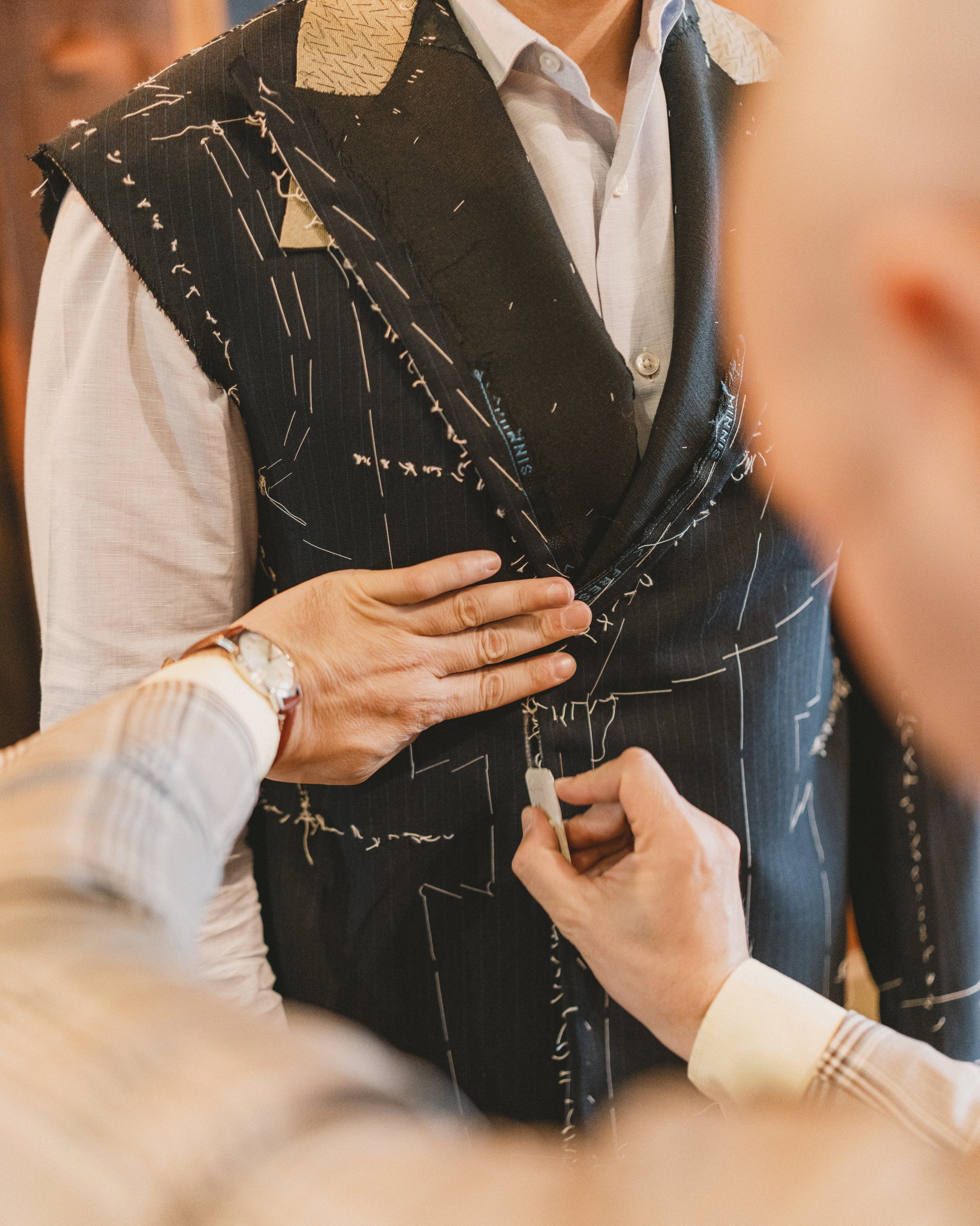 Close-up of a person pinning a name tag onto a dark, patterned vest worn over a white shirt during a formal event or conference.