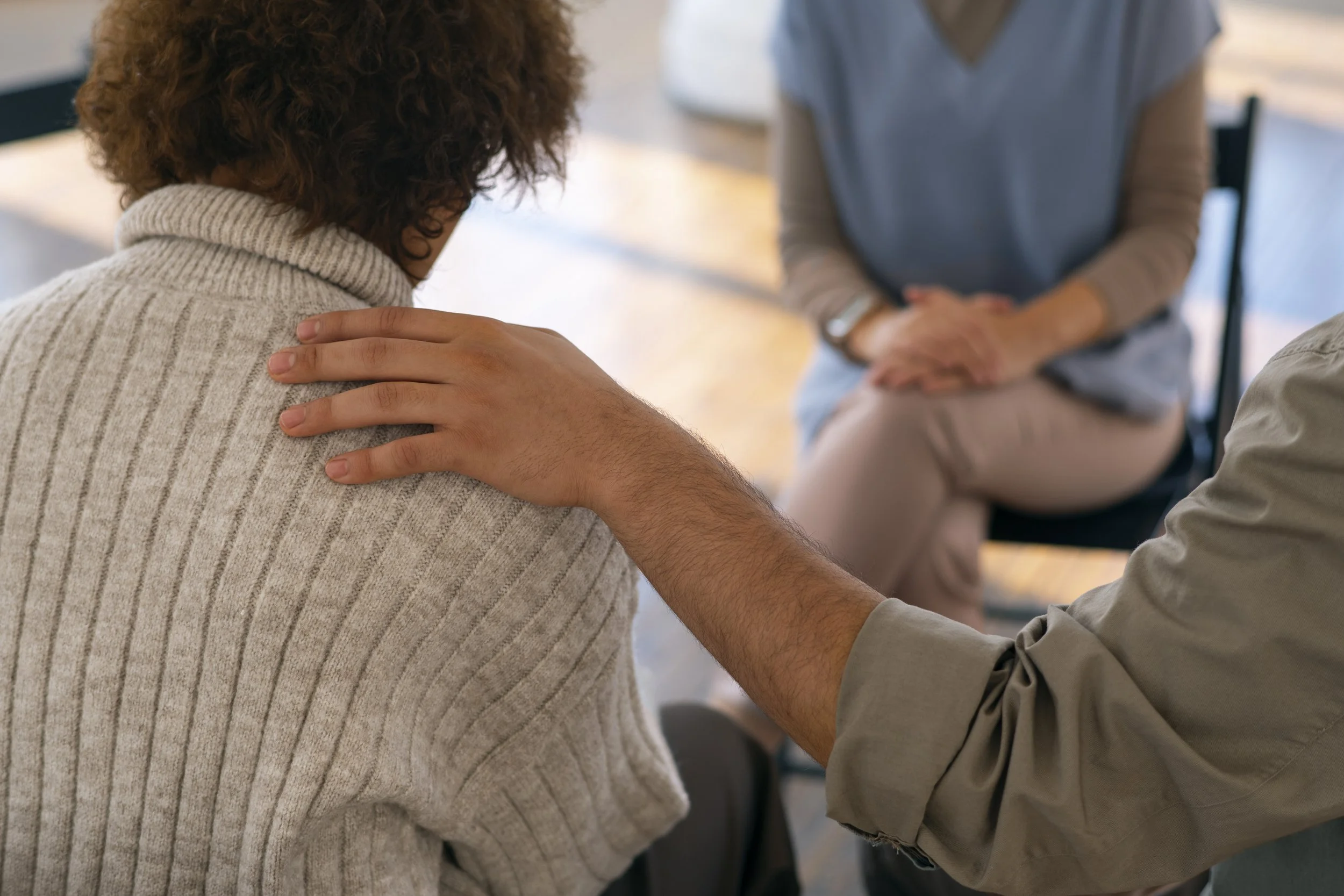 Two people sitting close, with one person's hand gently resting on the other's shoulder, suggesting comfort and support.