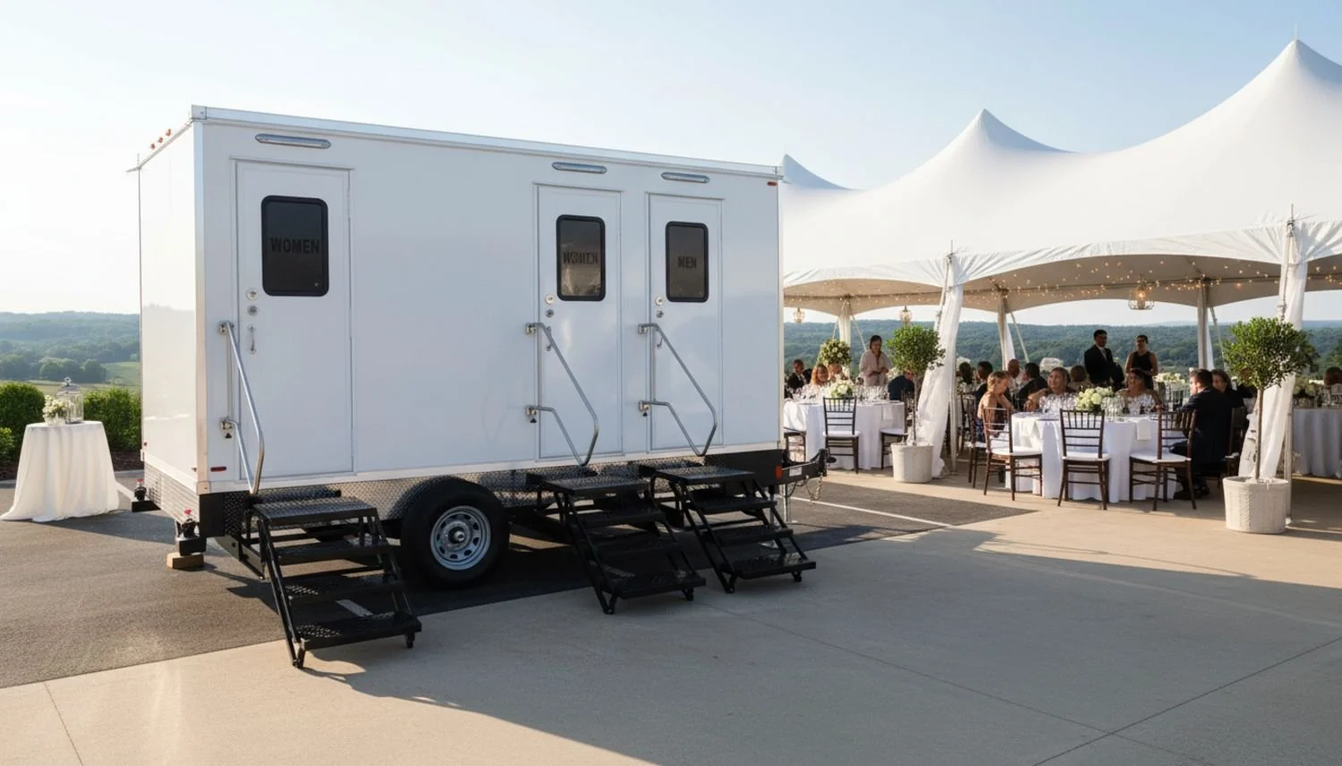 Portable restroom trailer with signs for women and men near a large outdoor tent with seated guests at a formal event.