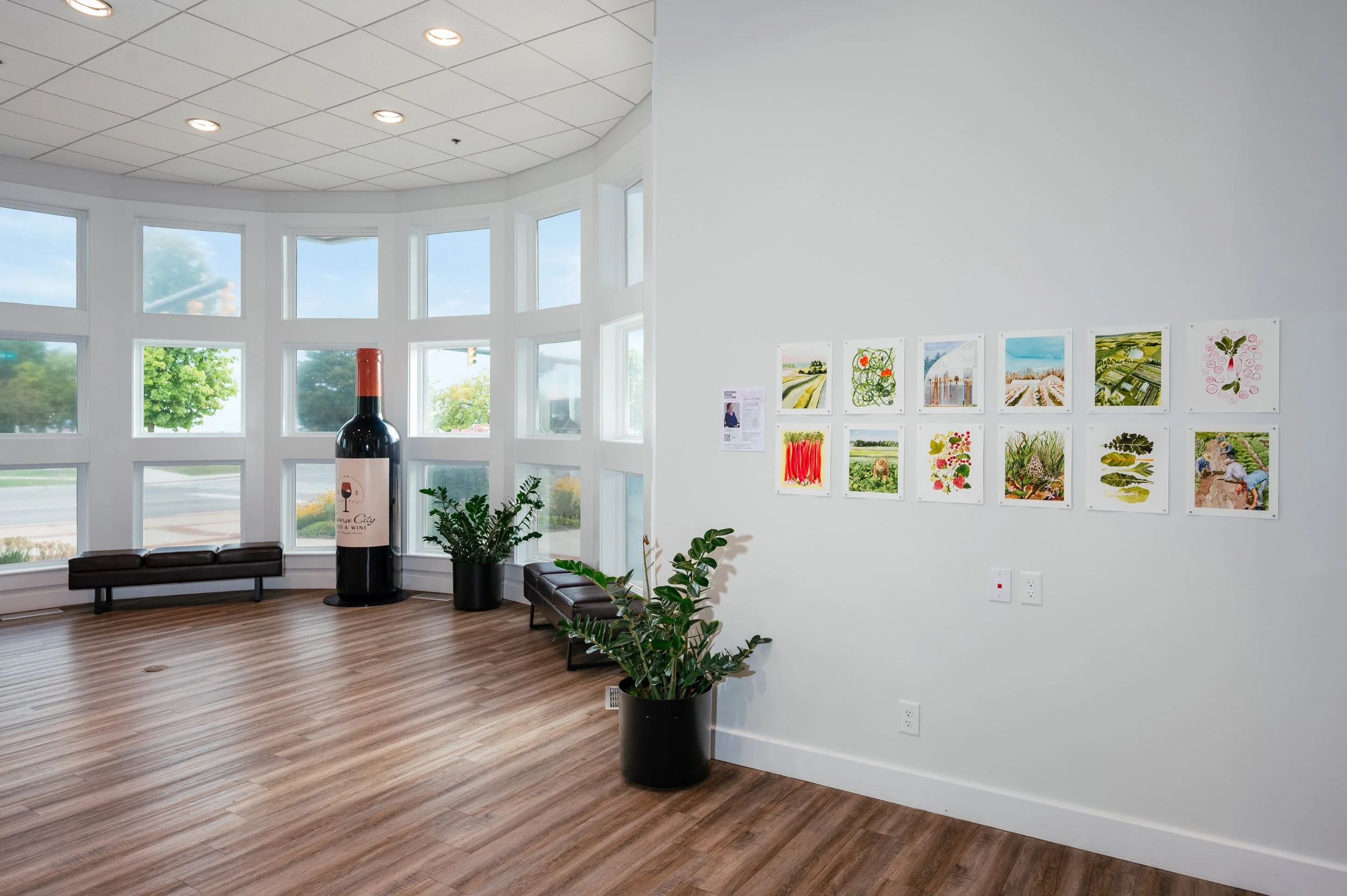 Interior of an art gallery with wooden support beams, white walls with framed artwork, a reception desk with poinsettia plants, and a hardwood floor.