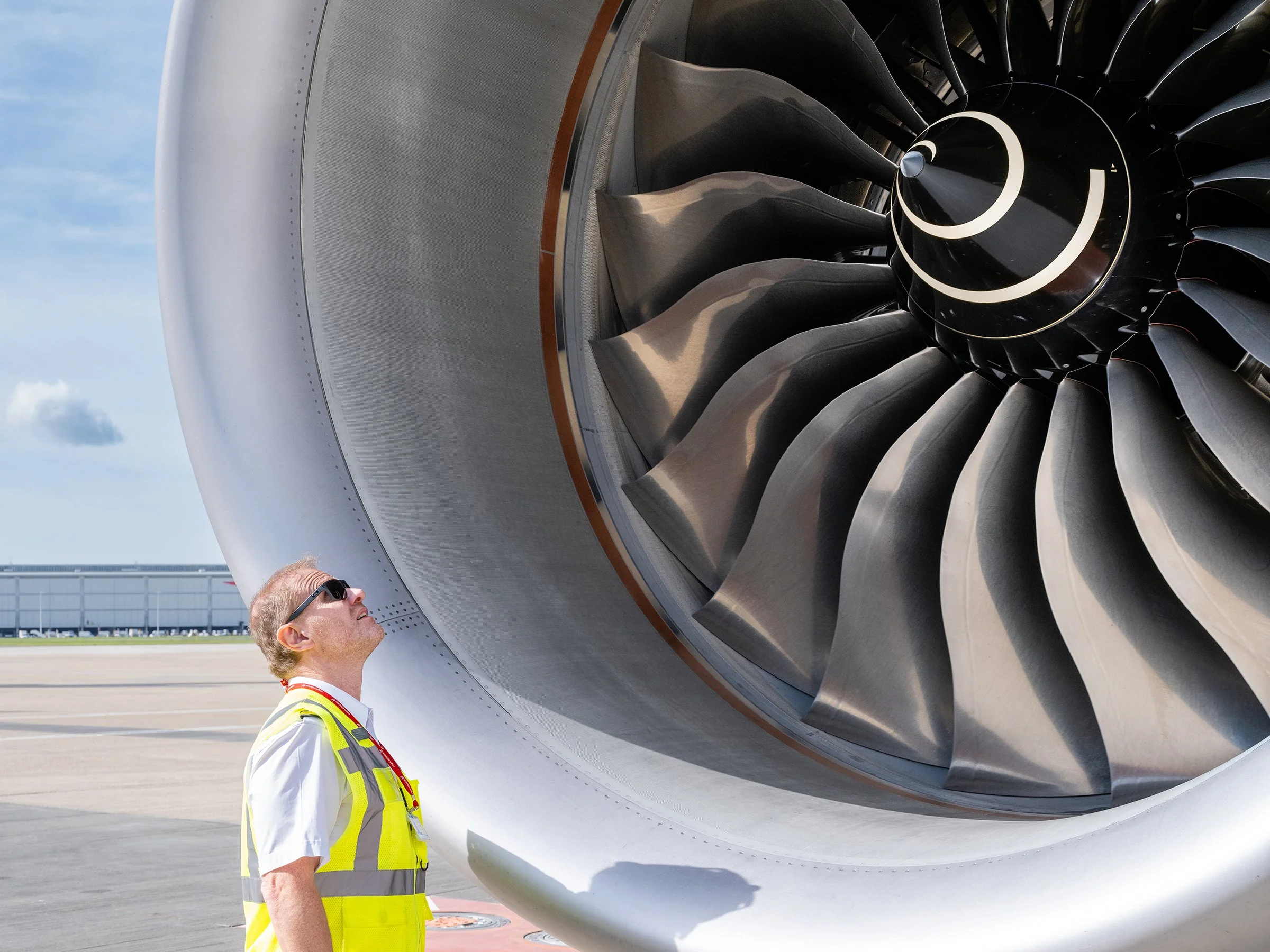 A person in sunglasses and a yellow safety vest inspecting an airplane engine during daytime.