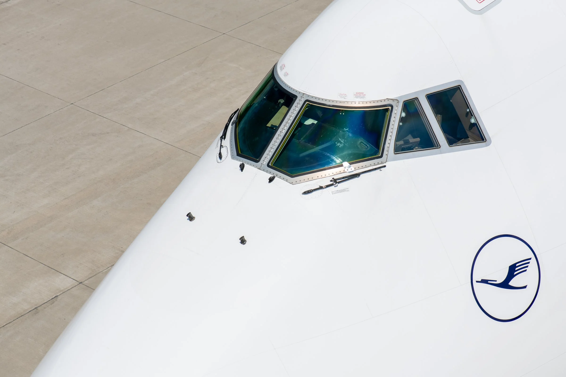 A close-up view of the cockpit and front section of a white airplane on the tarmac, with visible windows and aircraft markings.
