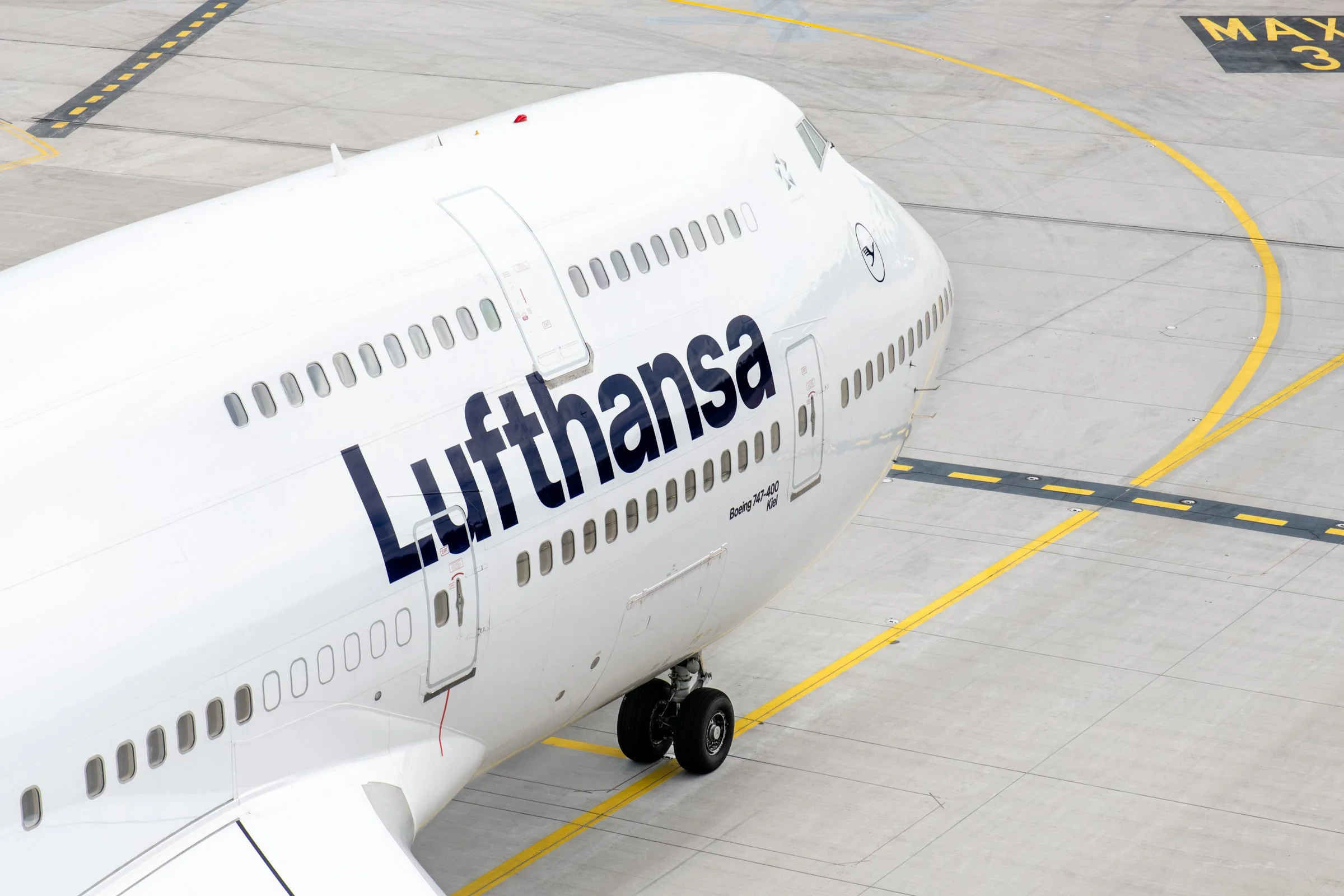Close-up of a large white airplane parked on an airport tarmac, with the partial logo and registration visible, and yellow markings on the ground.
