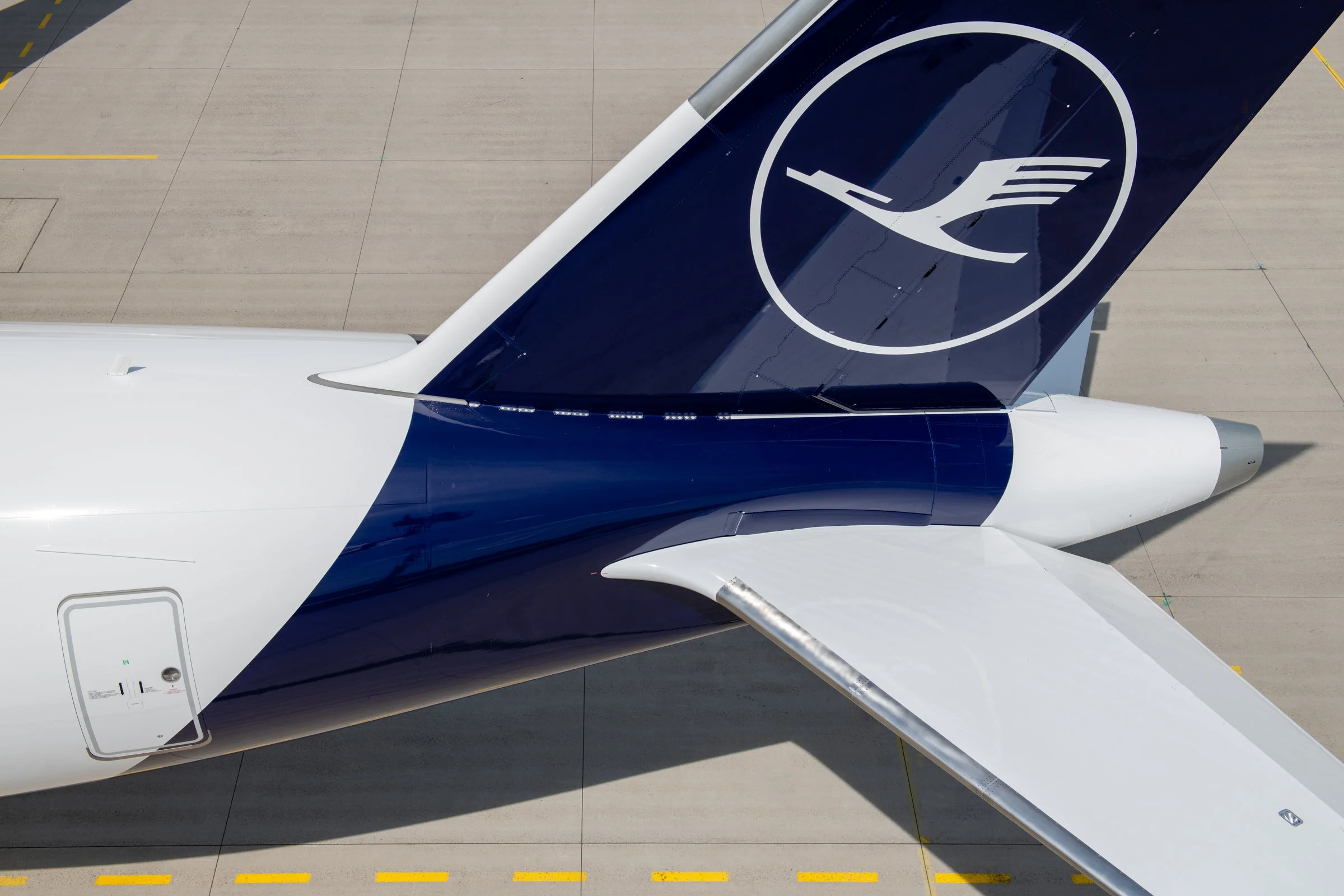 Top-down view of an airplane tail with the Lufthansa logo parked on the tarmac.