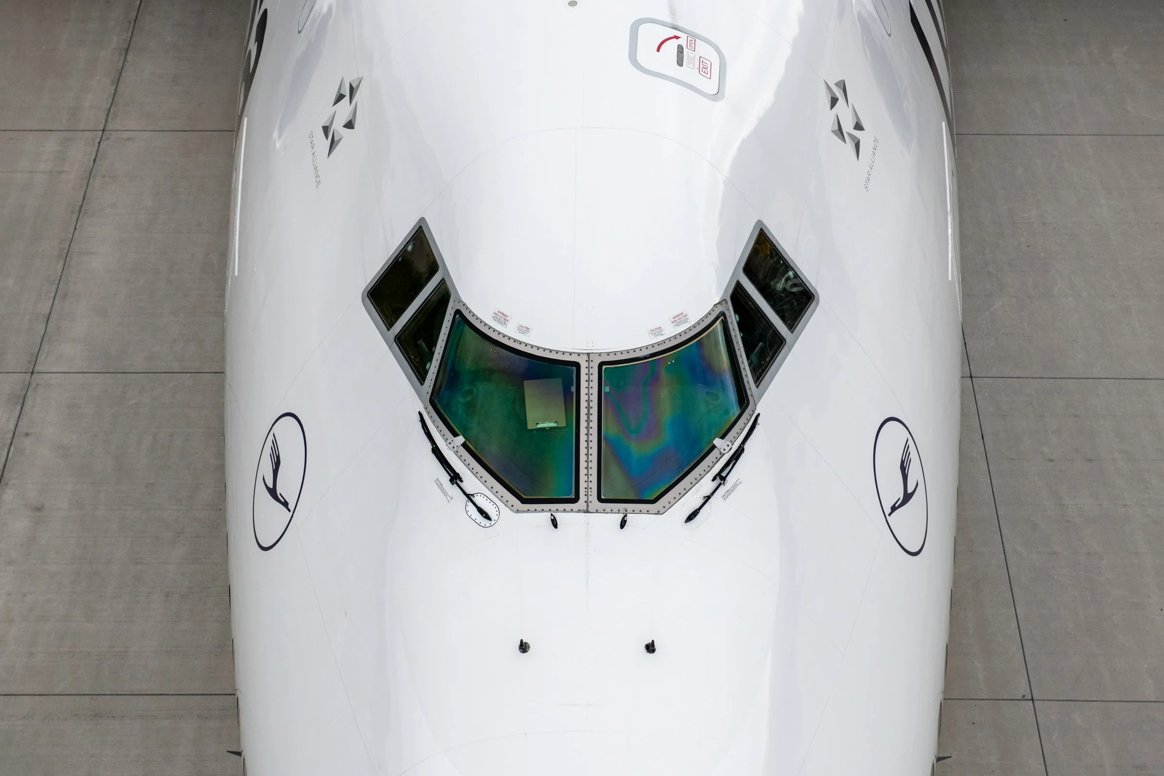 A white spacecraft with multiple windows and logos, positioned on a concrete surface, viewed from above.