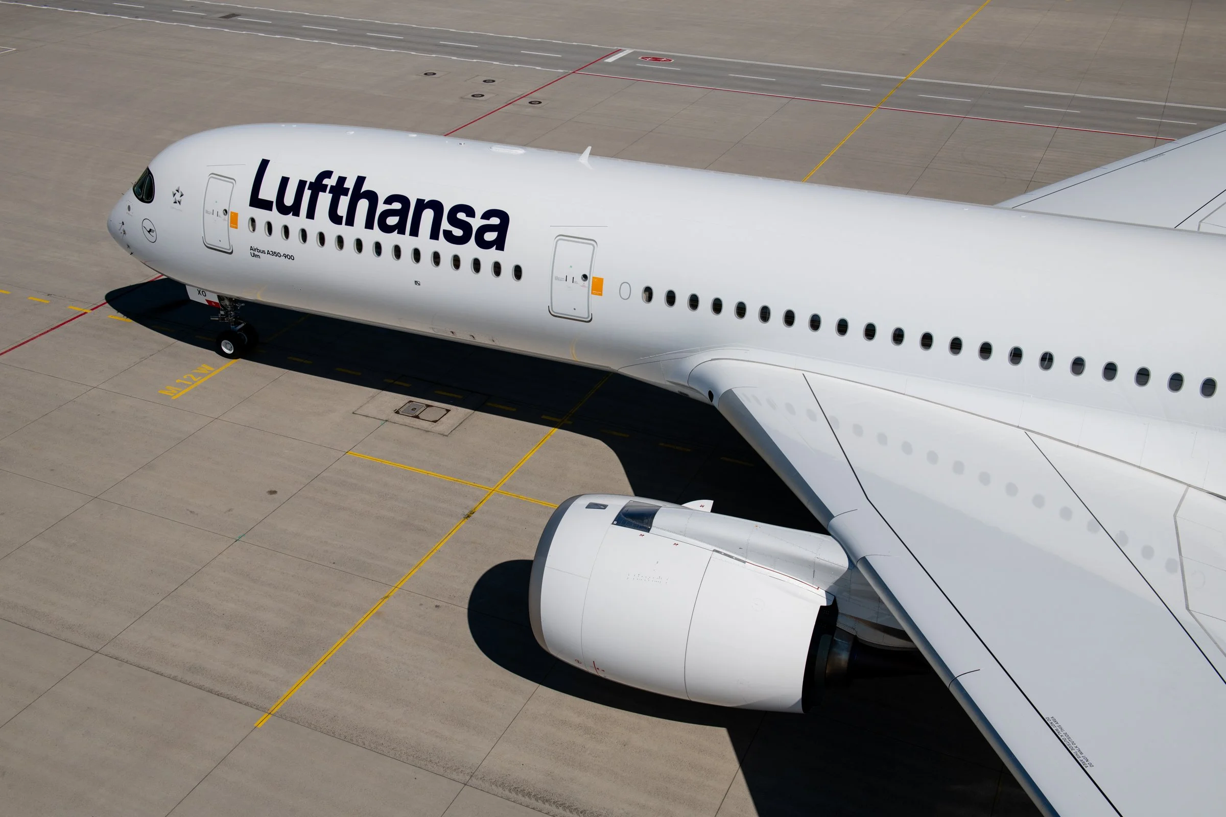 A white Lufthansa airplane parked on the tarmac, visible from above, with its nose and part of the wing in view.