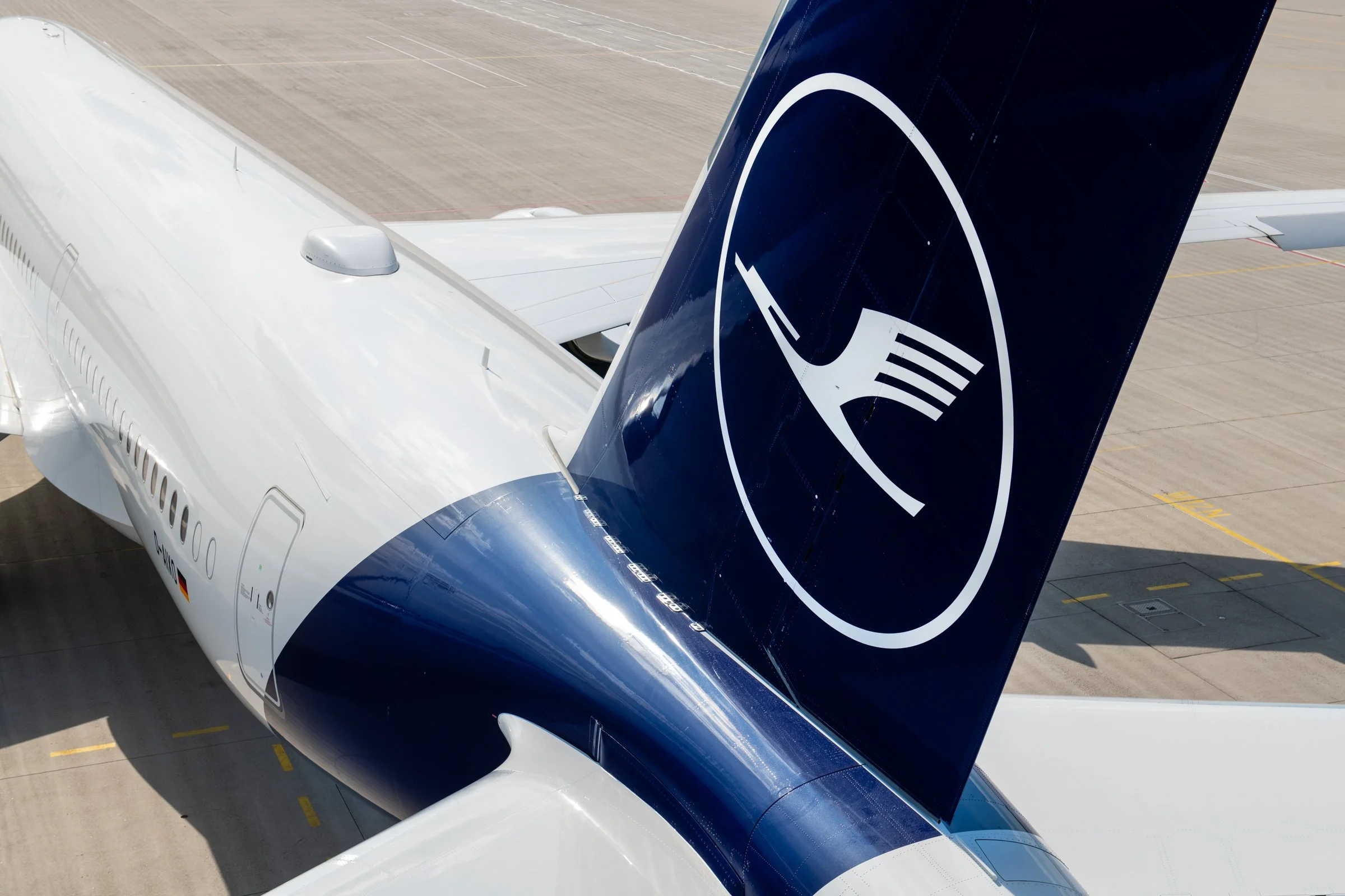 Close-up of an airplane's engine and a blue tail fin with a white logo, parked on an airport tarmac.
