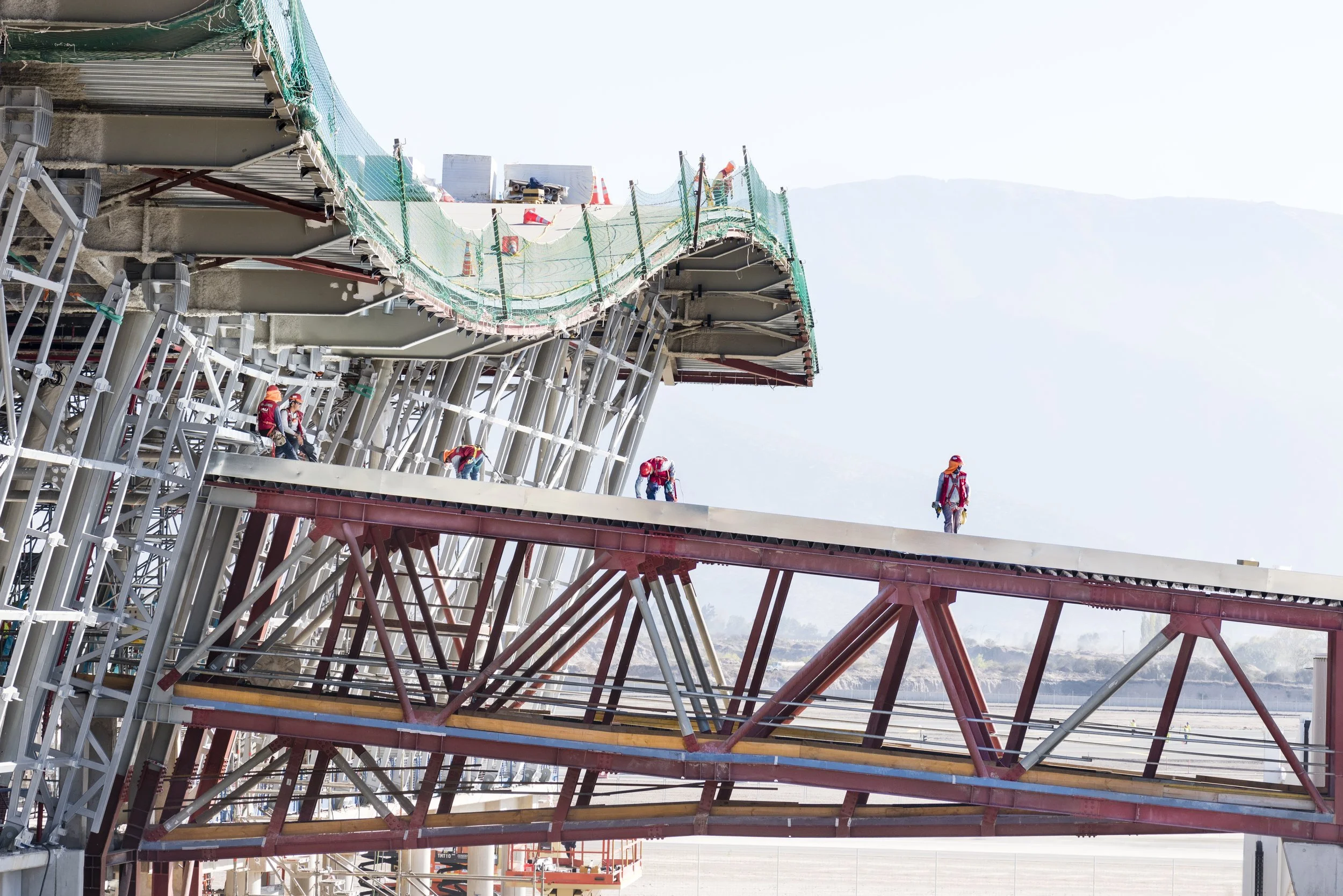 Construction workers on a bridge under construction, with steel beams, scaffolding, and safety equipment visible.
