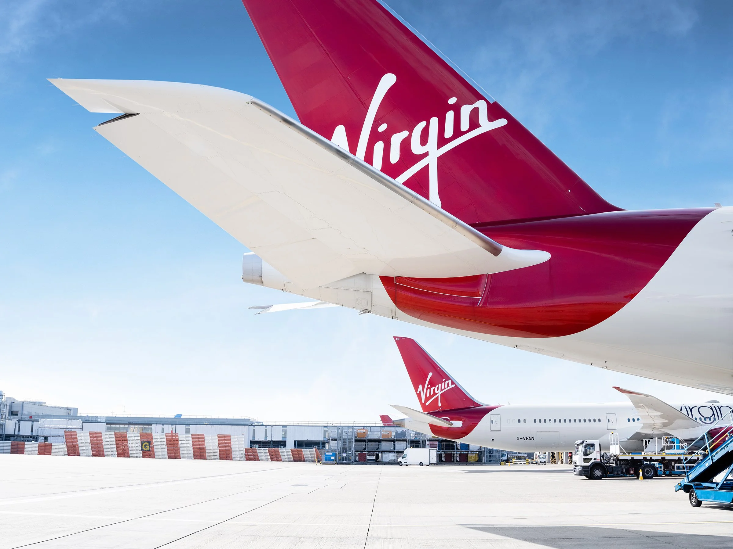 Multiple Virgin Airlines airplanes parked at an airport, with ground service vehicles and stairs nearby, under a clear blue sky.